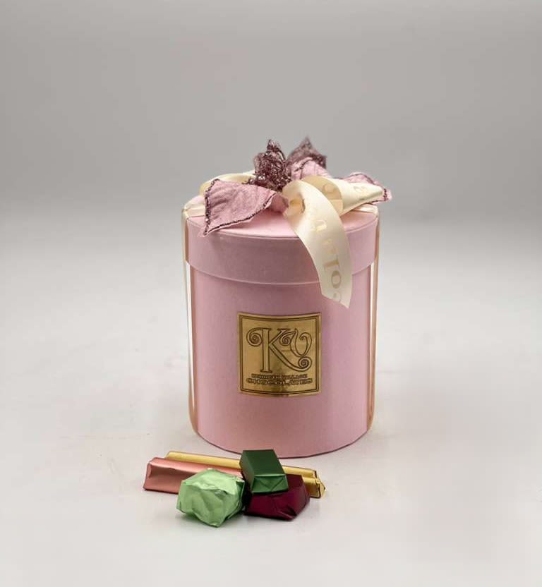 Pink gift box with ribbon and assorted chocolates in front