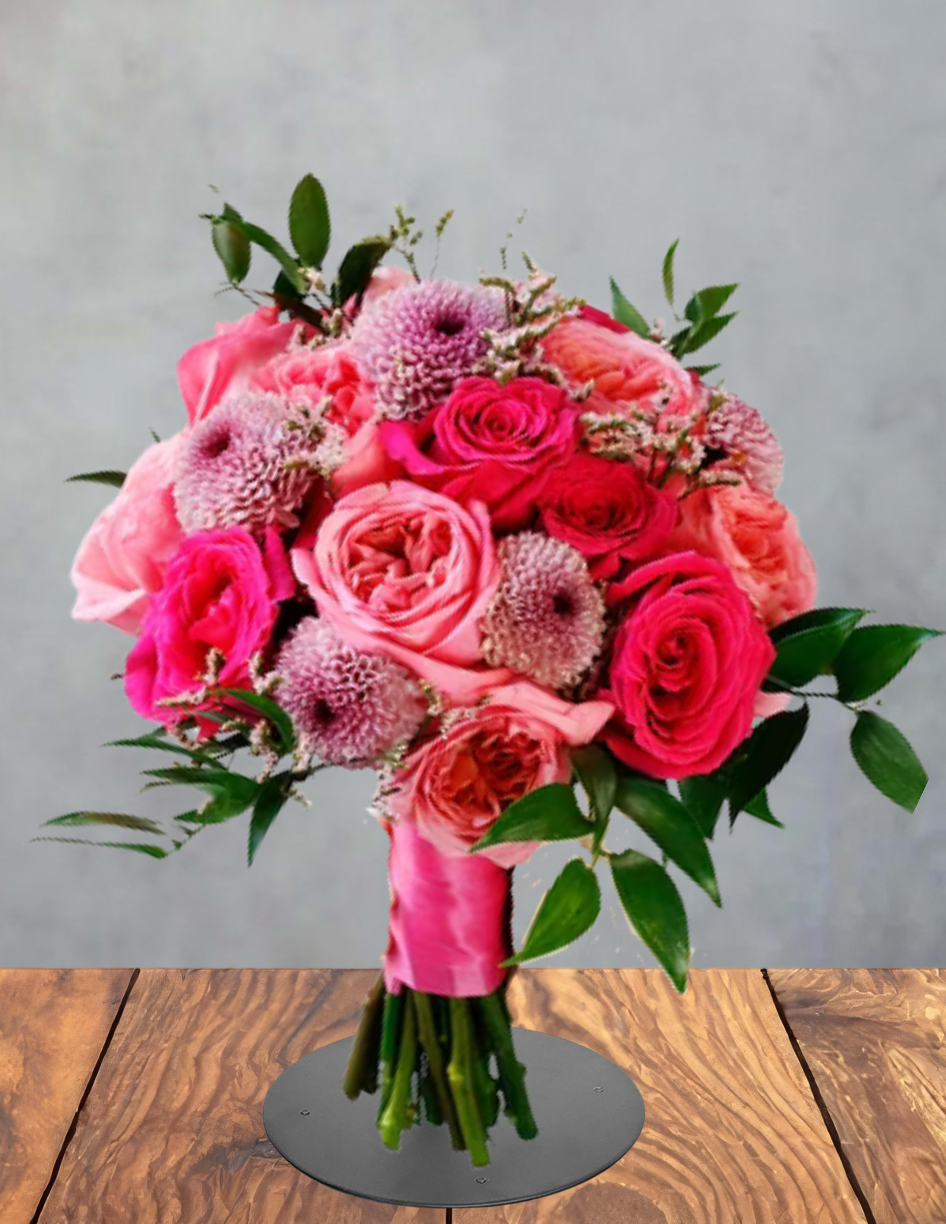 Prom Queen - A bold sunflower crown sits at the heart of this Prom Queen flower arrangement, a bright and cheerful choice for a birthday bouquet, congratulations, or a just-because gift. Sunflowers, pink roses, orange alstroemeria and purple filler blooms combine into a full, rounded display that reads festive and upbeat-the kind of bouquet that makes the person you're thinking of feel celebrated and uplifted.  The mixed-stem arrangement pairs sunny yellow, hot pink, lavender and orange tones with glossy greenery for lively contrast and texture. You'll find alstroemeria, stock, chrysanthemums and other seasonal fillers arranged tightly around the focal sunflower and clustered roses, with stems neatly wrapped in pale pink ribbon for a polished hand-tied look. The bouquet is presented on a display stand in photos to show its finished, gift-ready presentation.  Perfect for marking birthdays, anniversaries, congratulations or Valentine's moments, Prom Queen suits anyone who loves bold color and joyful energy. Care is simple: fresh-cut stems in clean water and a cool spot will extend blooms; if you'd like a wrapped bouquet for delivery, the arrangement arrives tied and ready to place or gift.