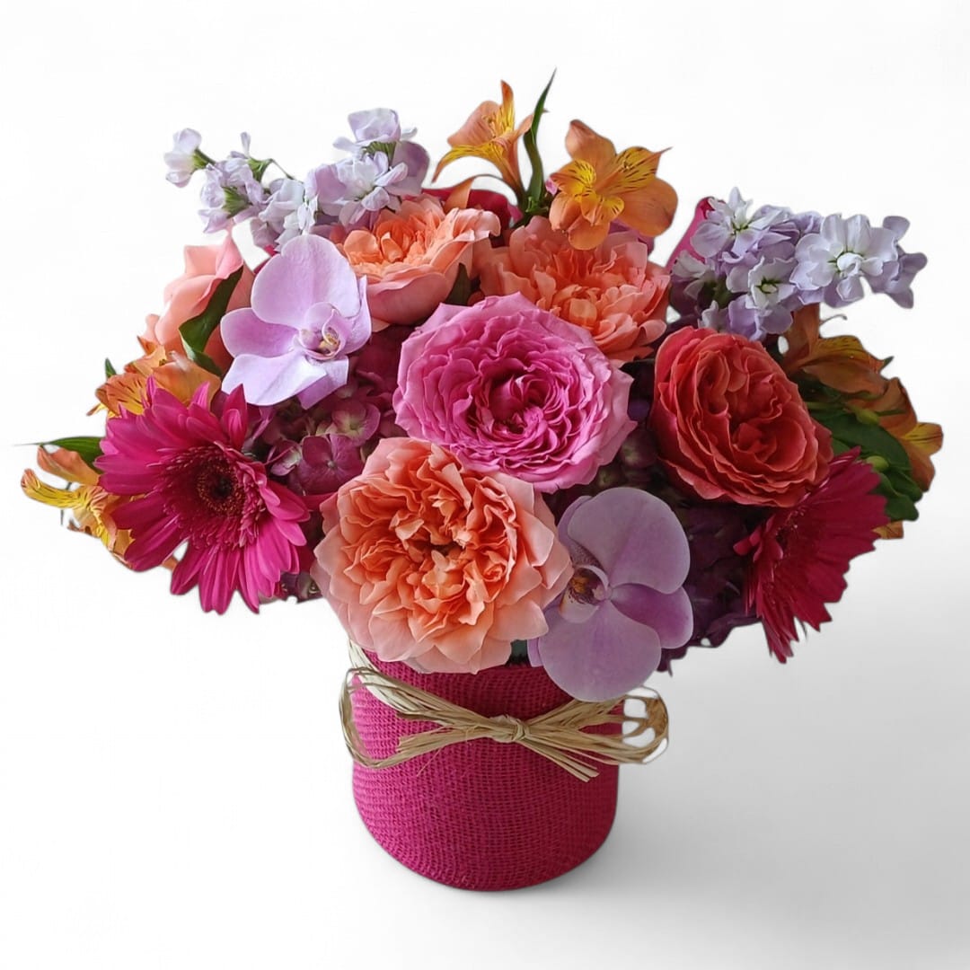 Mixed bouquet of pink, peach, and lavender flowers in a pink wrapped vase