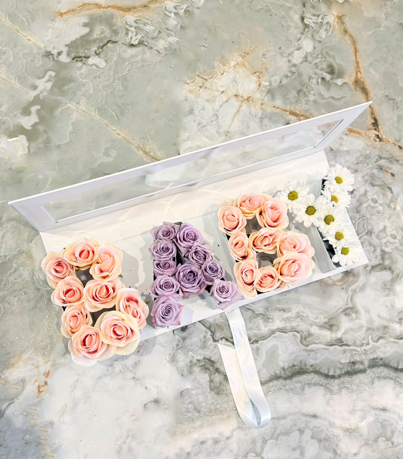 Floral arrangement spelling "A" with peach and lavender roses and white daisies