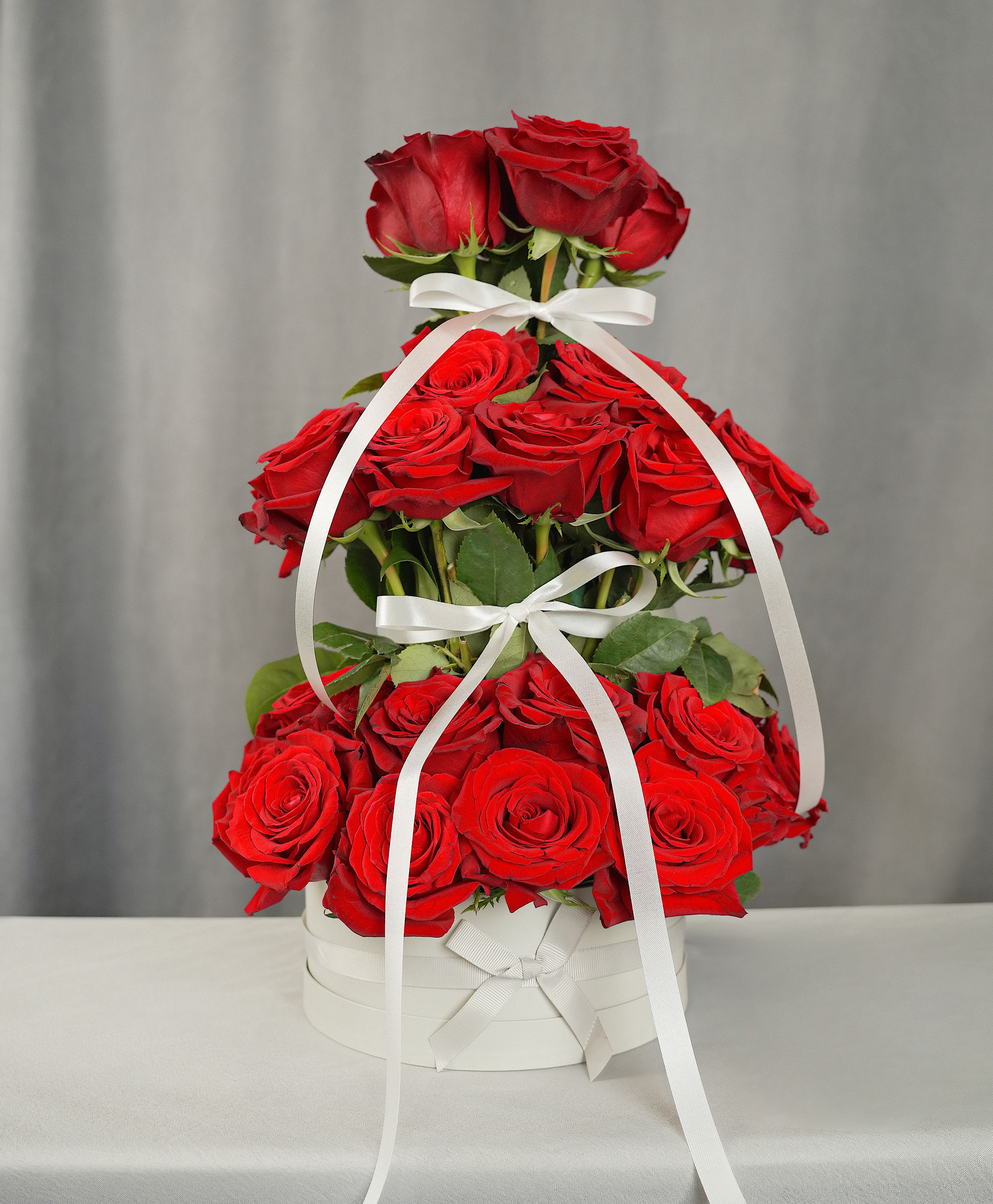 Tiered arrangement of red roses in a white box with ribbon bows