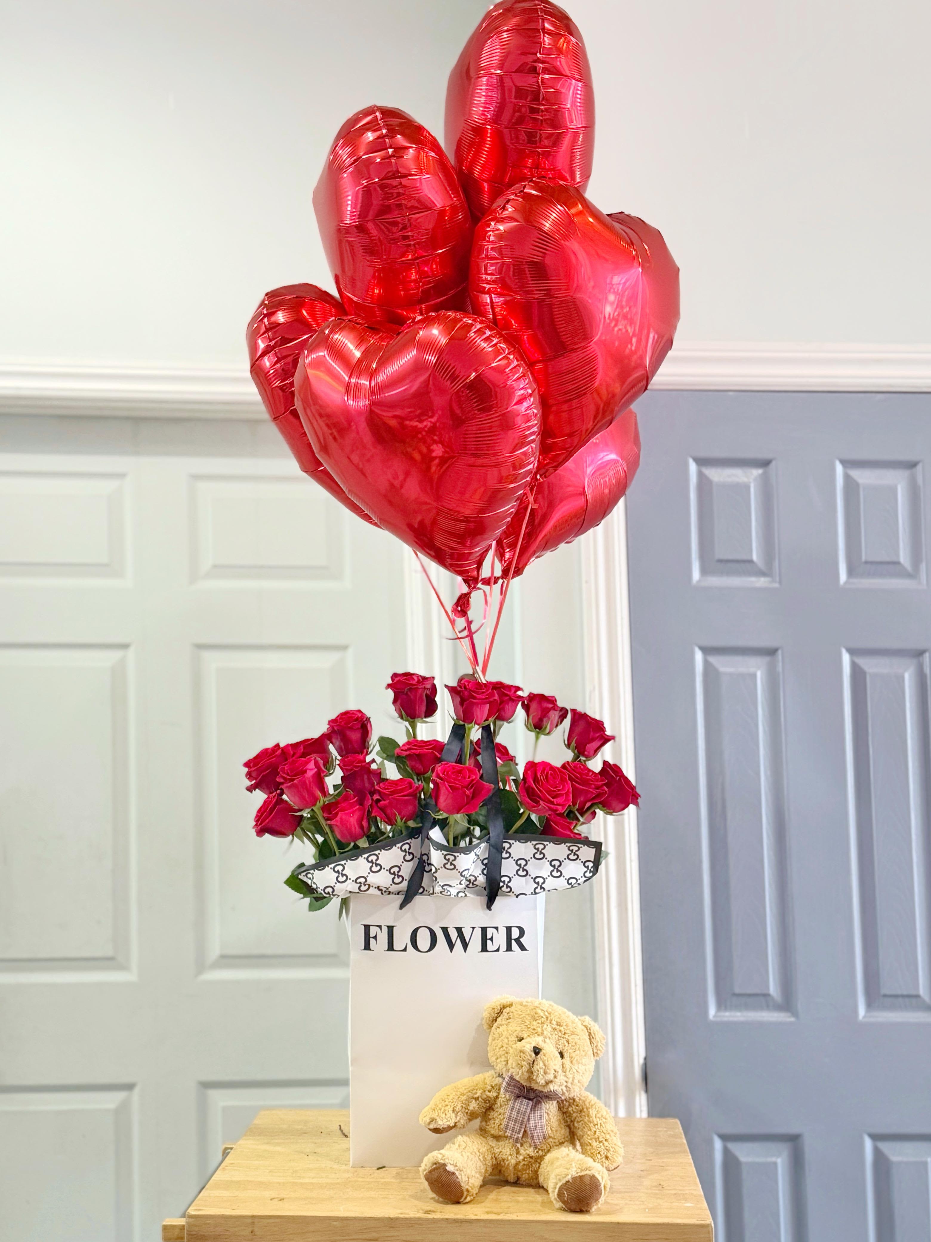 Red roses in a gift box with heart-shaped balloons and a teddy bear