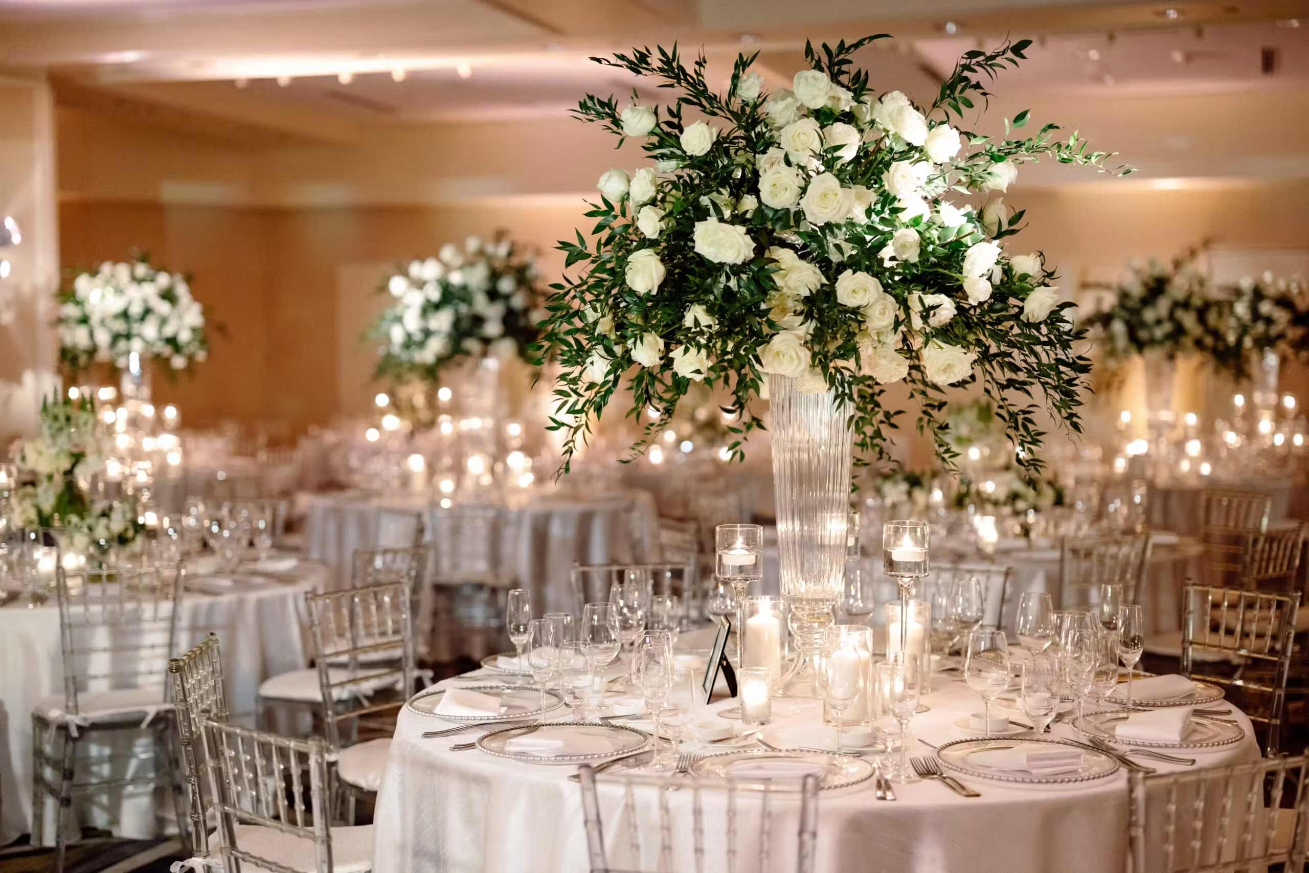 White rose centerpiece in a tall glass vase on a candlelit banquet table