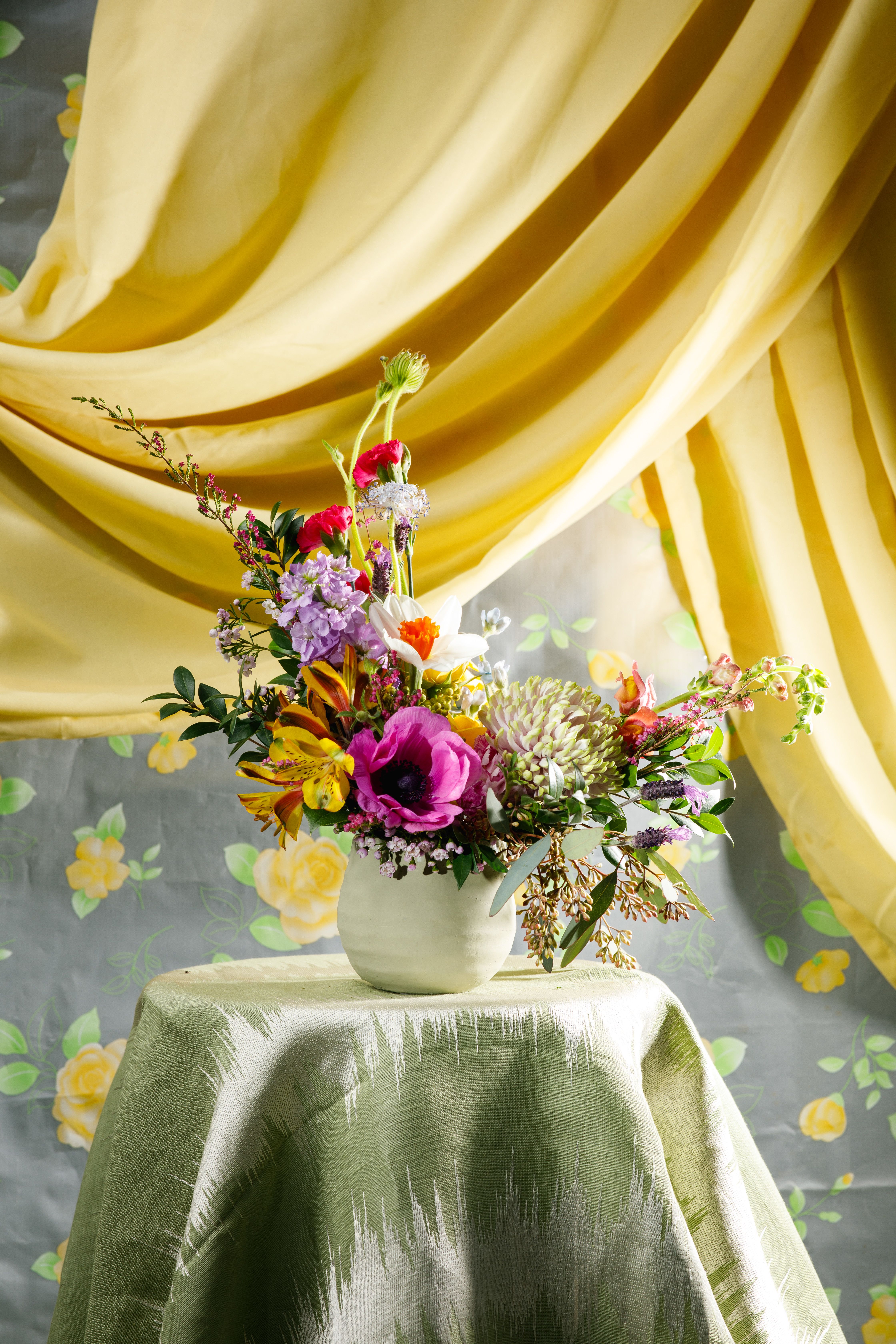 Asymmetrical mixed flower arrangement with pink, yellow, and white blooms in a small white vase.