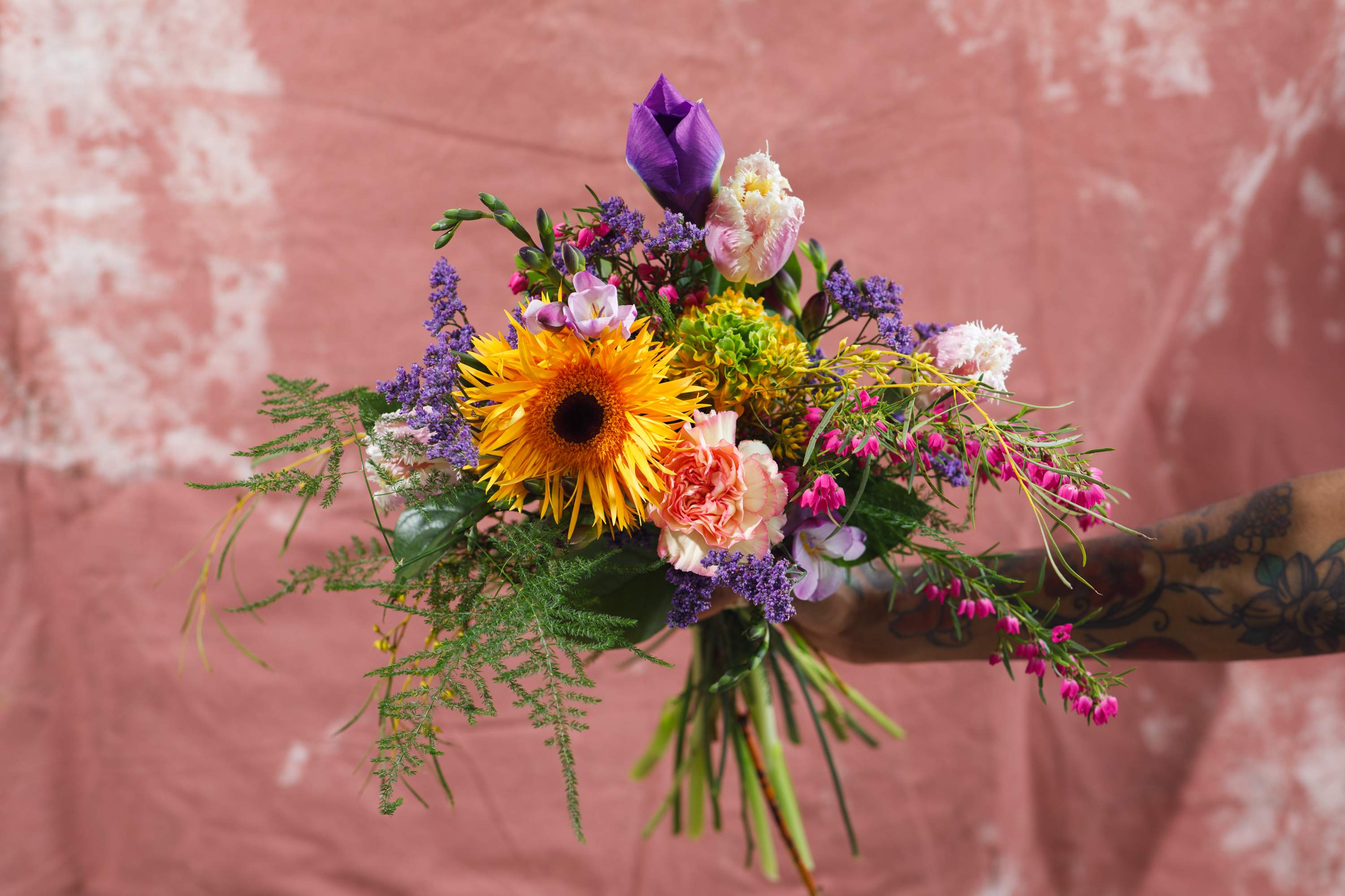 Handheld bouquet with a yellow sunflower, purple blooms, and pink flowers