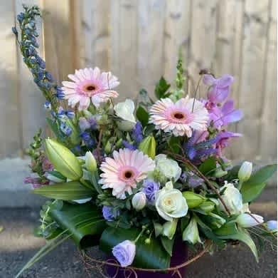 Mixed bouquet with pink gerbera daisies, white roses, and purple flowers in a basket