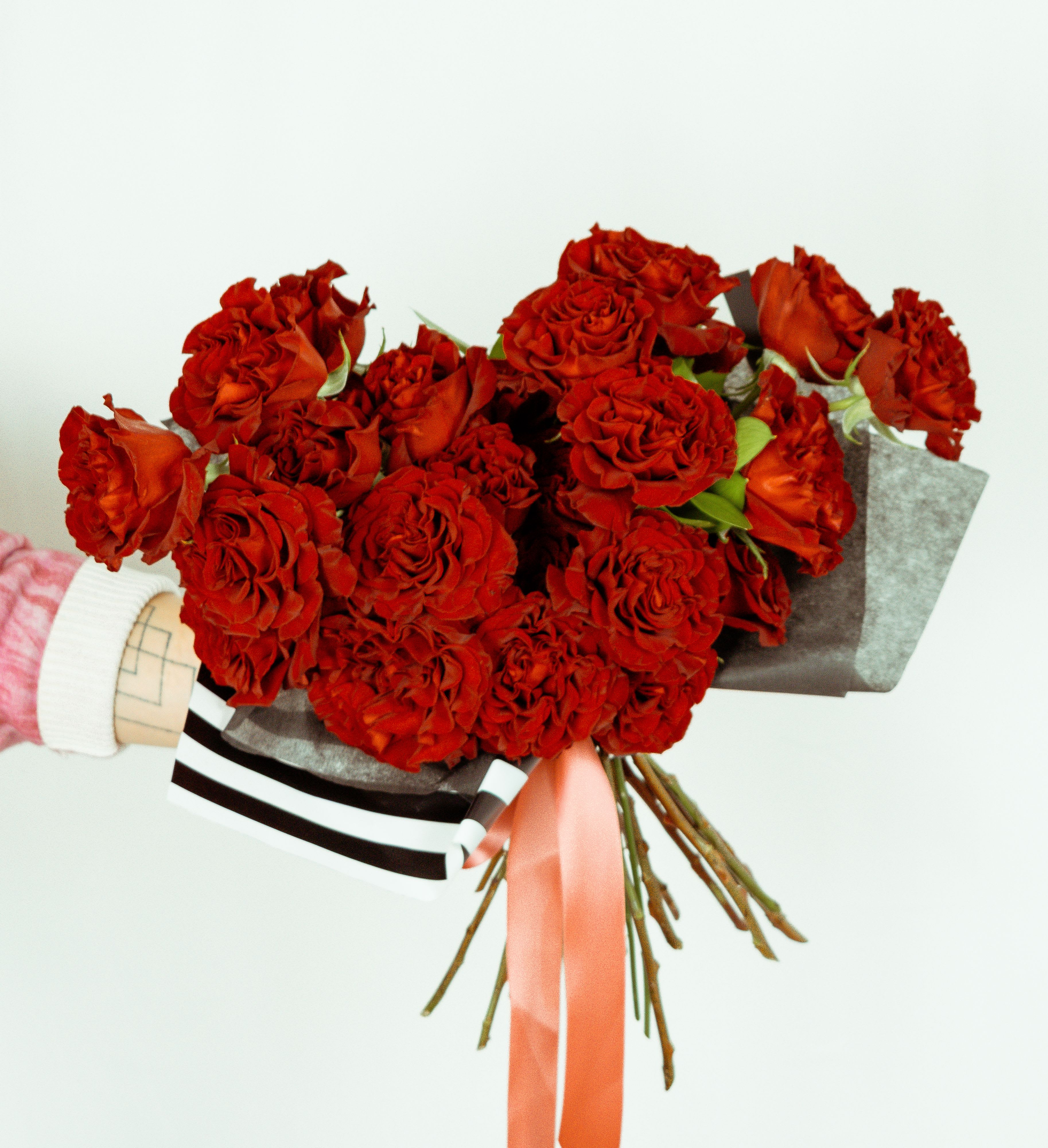 Bouquet of red roses wrapped in dark paper with a pink ribbon