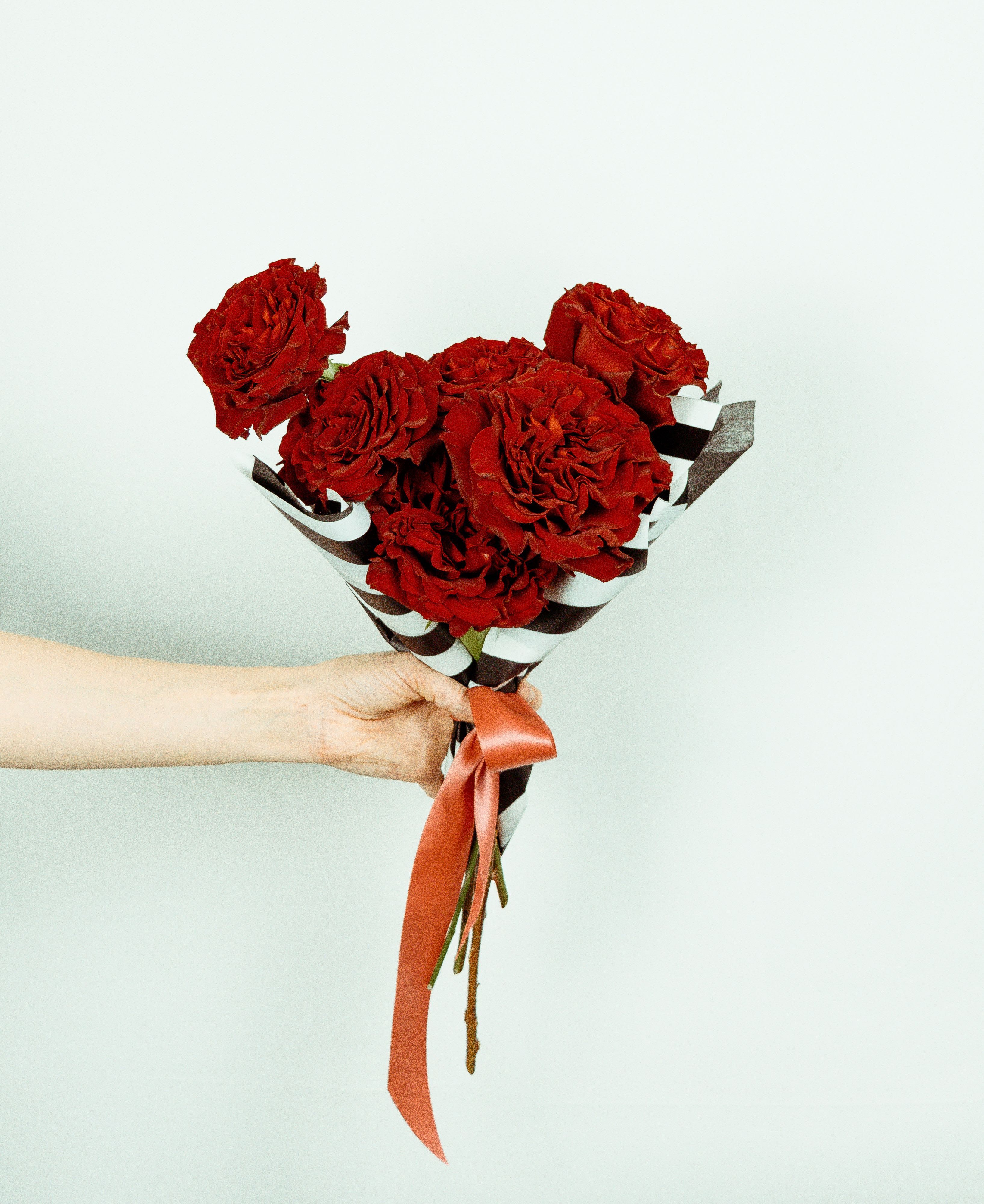 Handheld bouquet of red roses wrapped in striped paper with a ribbon