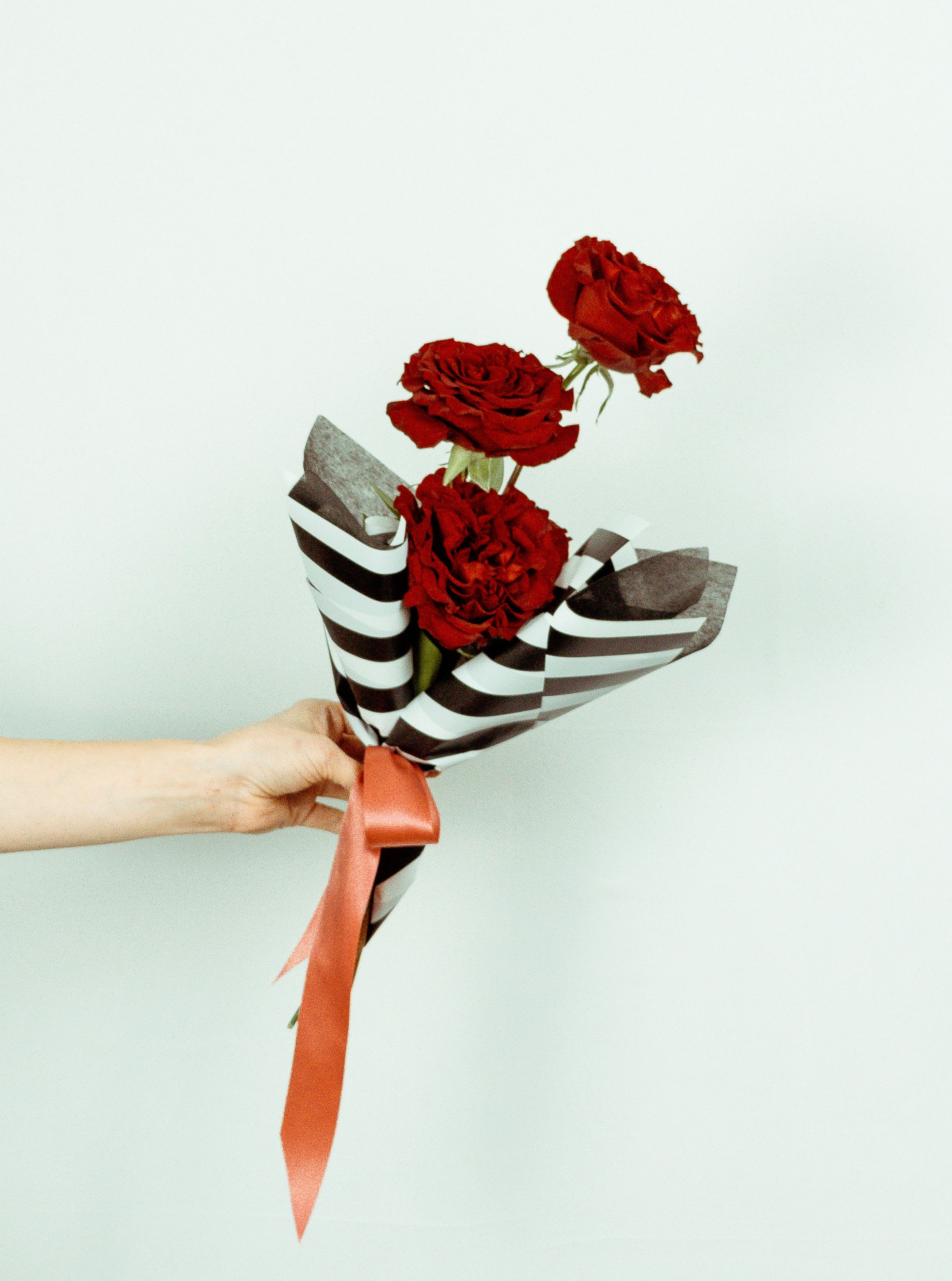Three red roses wrapped in striped paper with a ribbon