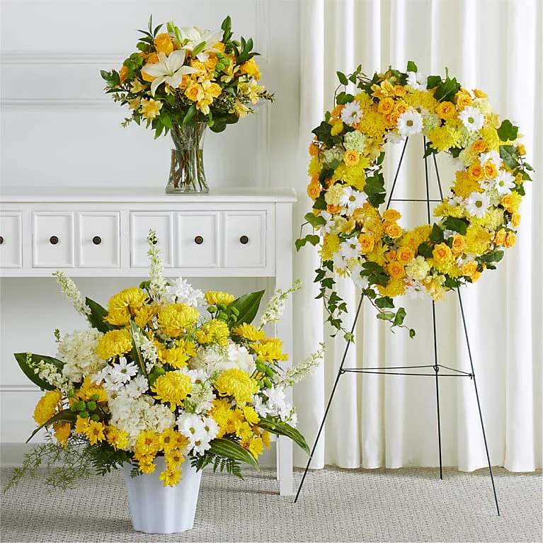 Golden Light Tribute Collection - A radiant expression of love, hope, and remembrance, the Golden Light Tribute Collection beautifully celebrates a life filled with warmth and joy. Designed with a vibrant blend of golden yellow blooms, crisp white flowers, and lush greenery, this coordinated set brings a sense of light and peace to any service.  Featuring an elegant casket spray, a standing wreath, and complementary arrangements, each piece is thoughtfully crafted to honor cherished memories while uplifting those in attendance. The yellow tones symbolize friendship, gratitude, and a life well-lived, while the white accents reflect purity and peace.  This harmonious tribute collection offers a comforting presence, creating a serene yet uplifting atmosphere that honors your loved one with dignity, beauty, and grace.