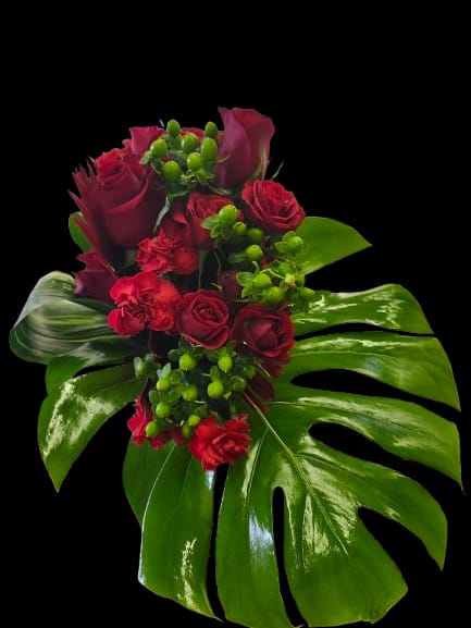 Power of Love - Deep, velvety red roses and clustered red carnations create an immediate, romantic impact in this compact flower arrangement - the perfect birthday bouquet or love-and-romance gift to make someone feel deeply cherished. The bold red-and-green contrast gives a lush, tropical edge that reads both dramatic and intimate; the person you're thinking of will notice the richness of the color and the confident, sculpted silhouette before anything else.  Glossy split tropical leaves and bright green berry-like accents frame the roses and carnations, keeping the composition tight and striking while adding texture and visual depth. This everyday arrangement works well for anniversaries, thank-you gestures, or simply saying "I'm thinking of you"; it arrives as a compact, ready-to-display piece that's designed to stand out on a table or bedside. To keep the flowers fresh, change the water every other day and trim stems slightly when re-cutting into a vase.