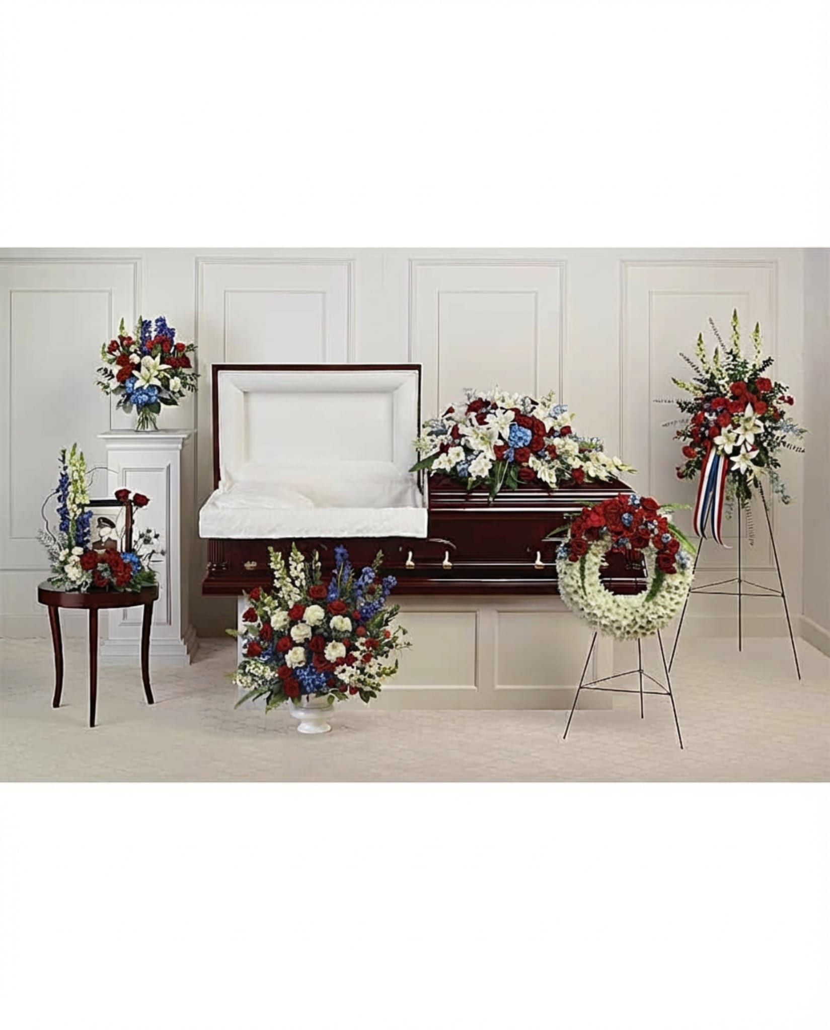 Patriotic Honor Tribute Collection - A dignified and heartfelt expression of honor and remembrance, the Patriotic Honor Tribute Collection pays tribute to a life of courage, service, and devotion. Designed in a classic palette of red, white, and blue, this collection reflects strength, respect, and enduring pride.  Featuring an elegant casket spray, a standing wreath with patriotic accents, and coordinating arrangements, each piece is thoughtfully crafted with roses, lilies, and seasonal blooms, complemented by lush greenery. The bold colors symbolize bravery, purity, and loyalty—creating a meaningful tribute for a loved one who will always be remembered with honor.  This striking collection offers a powerful and respectful presence, honoring cherished memories with dignity, gratitude, and lasting reverence.