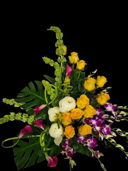 Vortex - Bright yellow roses swirl with deep purple orchids and pink calla lilies in a striking mixed bouquet perfect for birthday bouquets, congratulations, or thank-you gifts. Designed to feel celebratory and upscale, this flower arrangement makes the person you're thinking of feel seen-vivid color contrast and tall, graceful lines create an immediate impression of joy and appreciation.  Clusters of yellow roses balance rounded white blooms, coral-pink callas, and sculptural orchids amid large tropical-style leaves and arching green accents, giving the arrangement strong height and a lush, layered spread. The overall effect is bold yet refined, an everyday mixed bouquet elevated by tropical foliage and dramatic color pops. Order notes: this piece arrives ready to display and suits recipients who enjoy vibrant, contemporary floral statements.