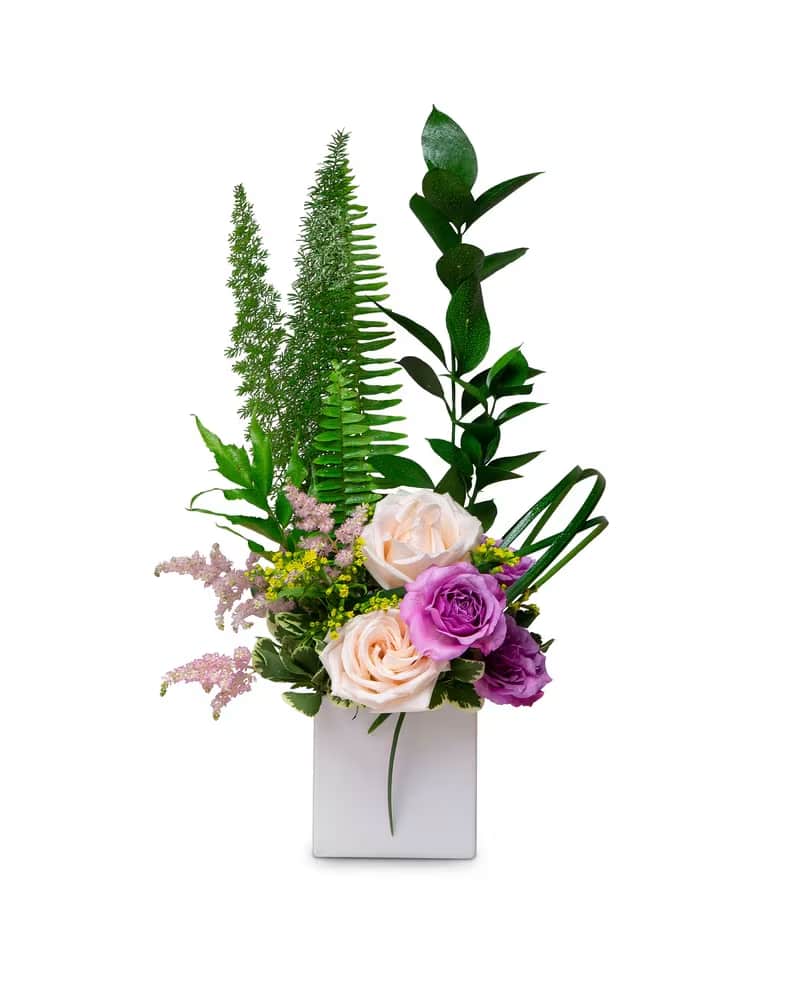 Spring Has Sprung - A sweet spring arrangement with a tall narrow design of blooms in pink, yellow, peach, and lavender enhanced with Florida foliage like lily grass, foxtail fern, sword fern, Florida ruscus, pittosporum designed in a white cube appropriate for an end table or edge of a desk.