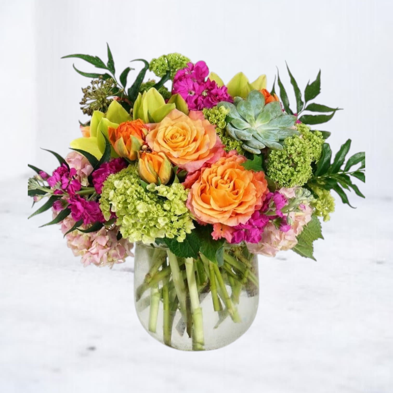Bravura - A vibrant composition of layered color and texture, this garden-inspired arrangement brings together succulents, premium roses, seasonal blooms, and delicate accent flowers in a lush, low design. Golden and violet tones blend effortlessly, creating depth and movement from every angle.  Designed in a modern glass vase, this arrangement feels fresh, artistic, and full of life—perfect for birthdays, celebrations, thank-you gifts, or simply brightening someone’s space. Each bloom is thoughtfully placed to create a natural, abundant look while maintaining a refined, elevated feel.  Available for same-day flower delivery in Houston, Magnolia, The Woodlands, Montgomery and surrounding areas. Flower varieties may vary slightly based on seasonal availability while preserving the overall color palette and style.