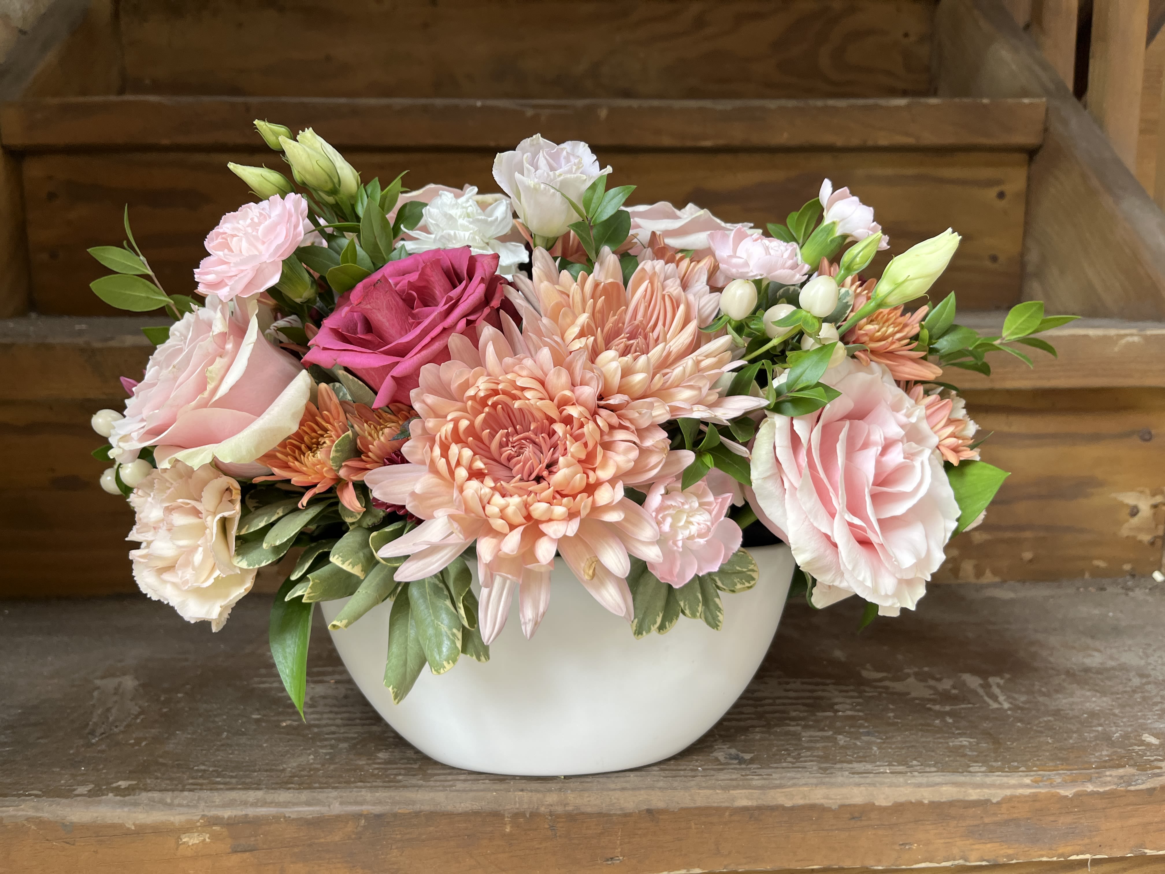 Pink and peach mixed flower arrangement in a white bowl vase