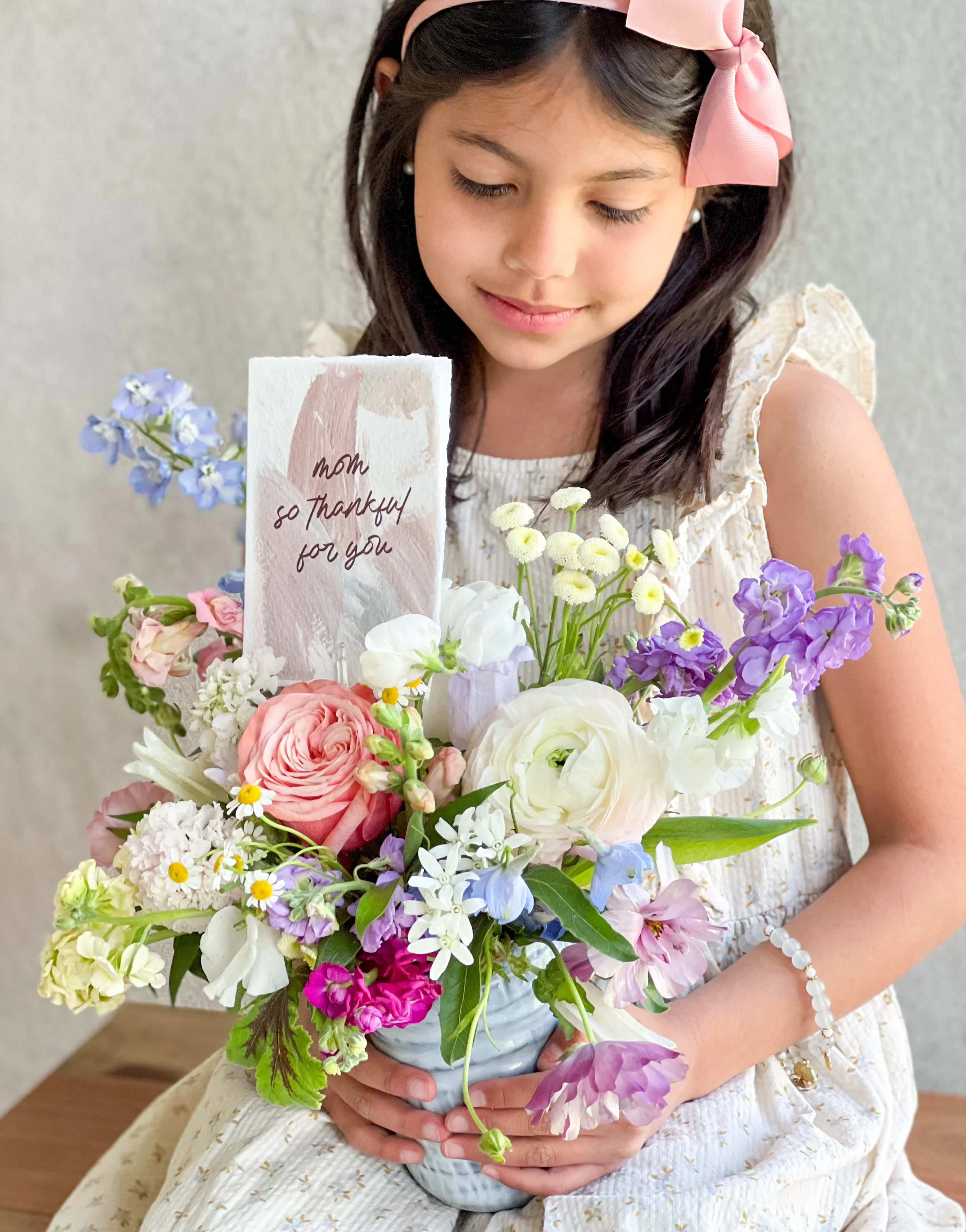 Girl holding a pastel mixed flower arrangement with a thank-you card