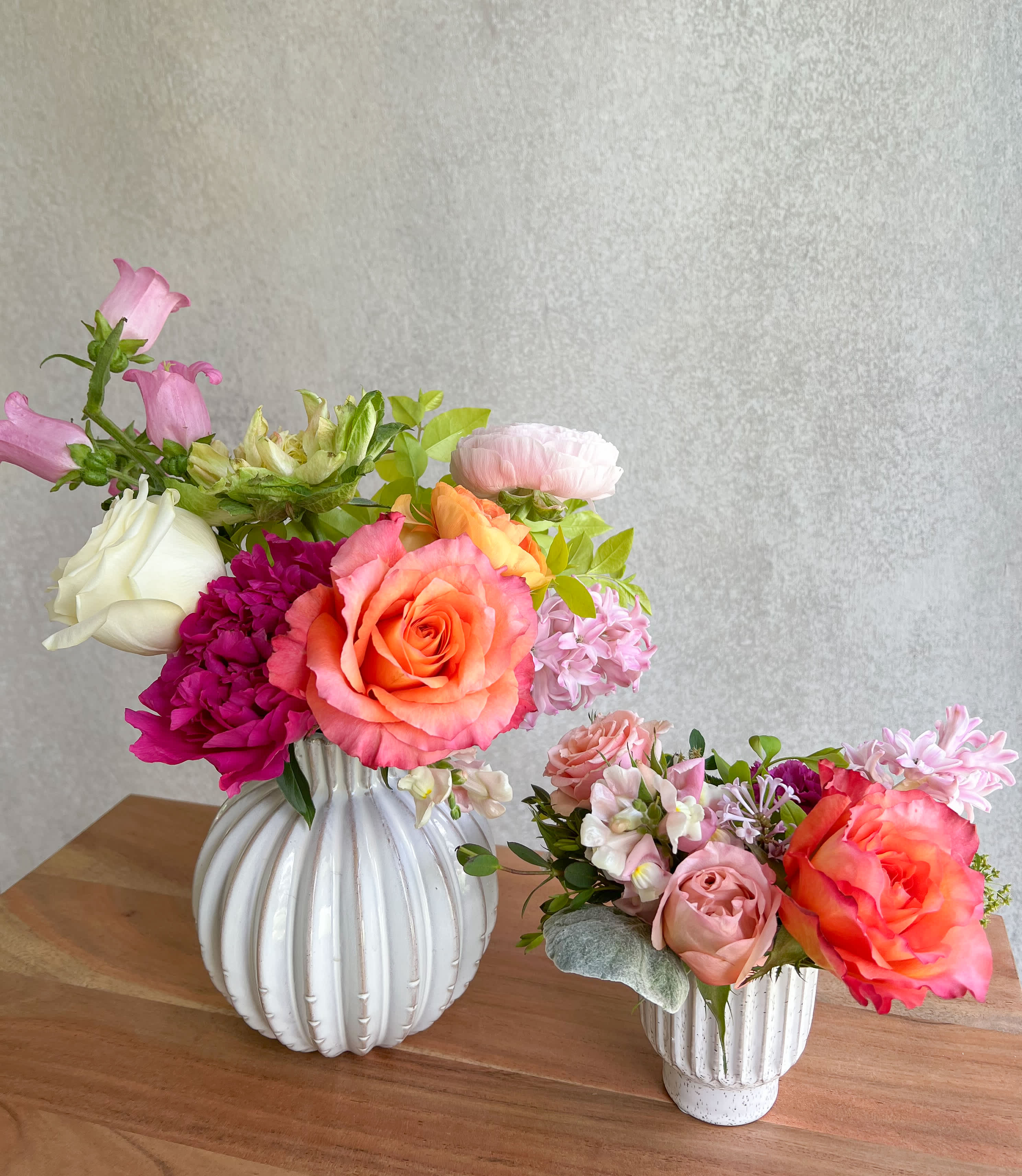 Two colorful floral arrangements in white vases on a wooden table
