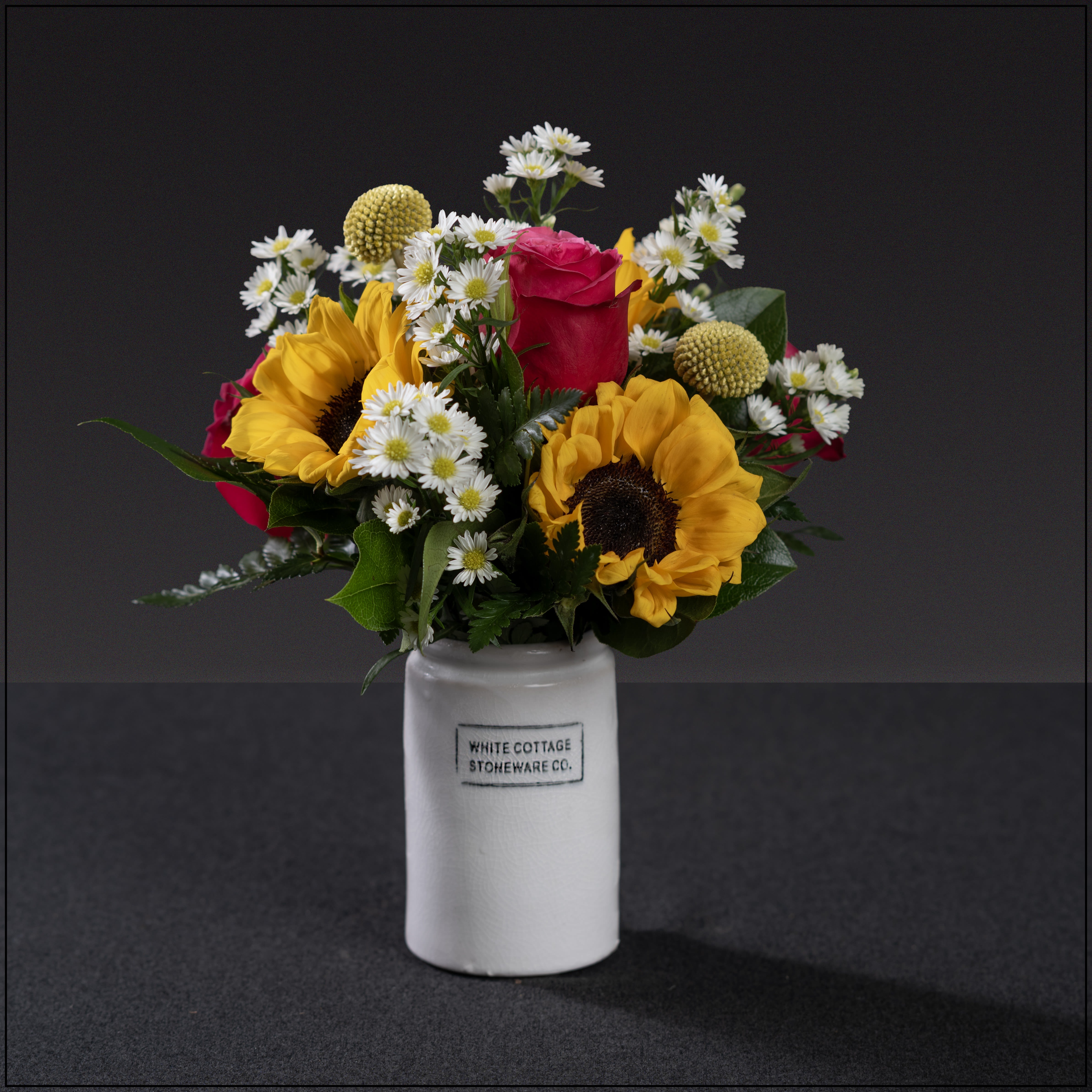 Cottage Stoneware -  A fun mix of sunflowers, roses, asters and craspedia in a stamped stoneware vase.
