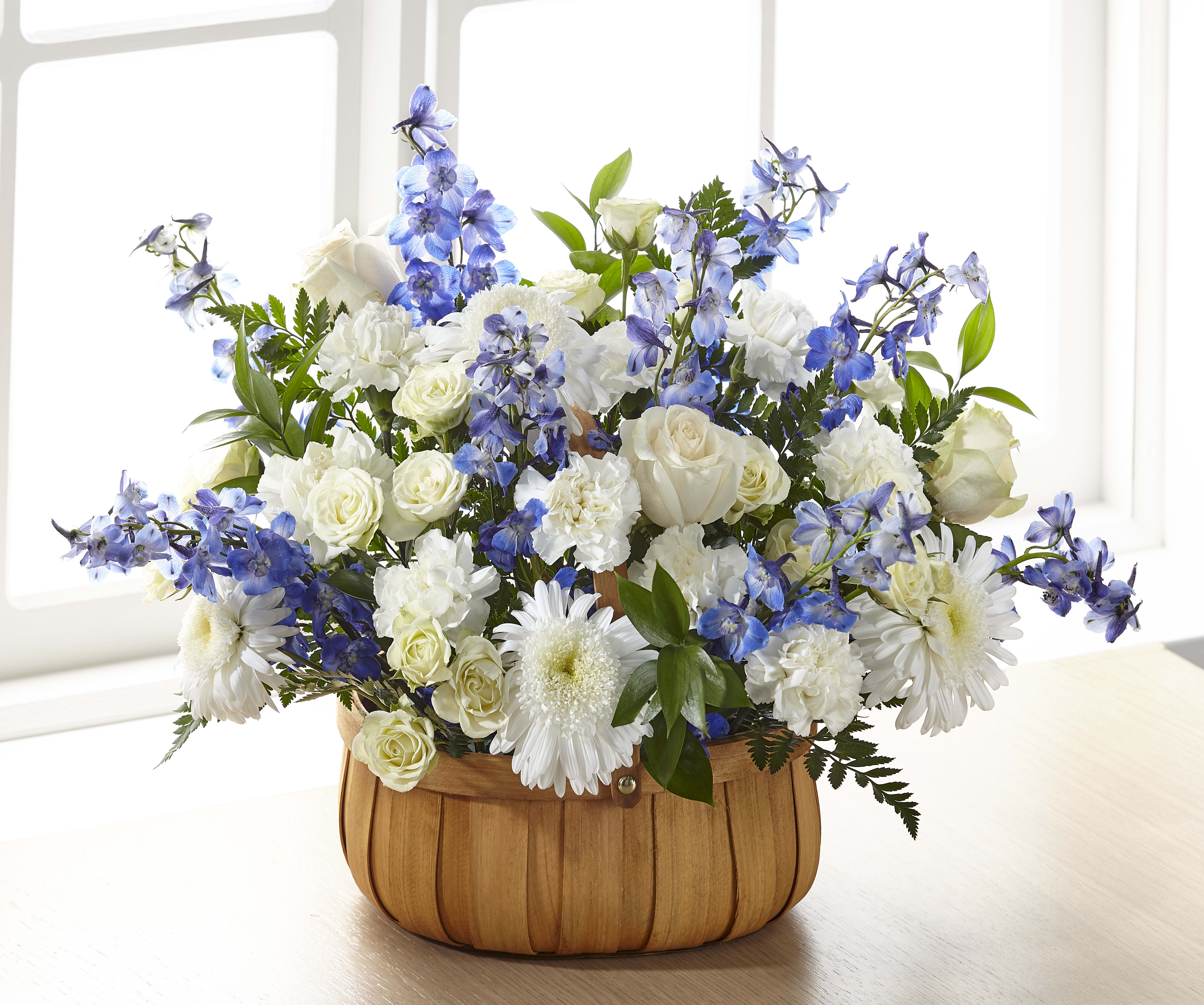 Basket arrangement of white roses, carnations, and daisies with blue delphinium.