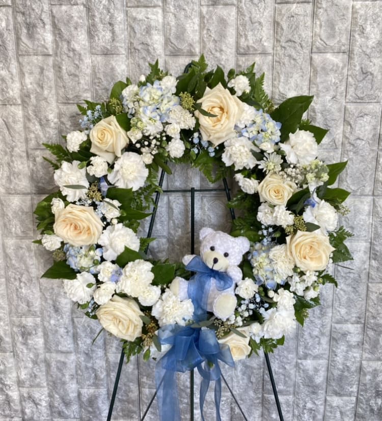 Heart-shaped floral wreath with cream roses, white flowers, and a blue ribbon on an easel