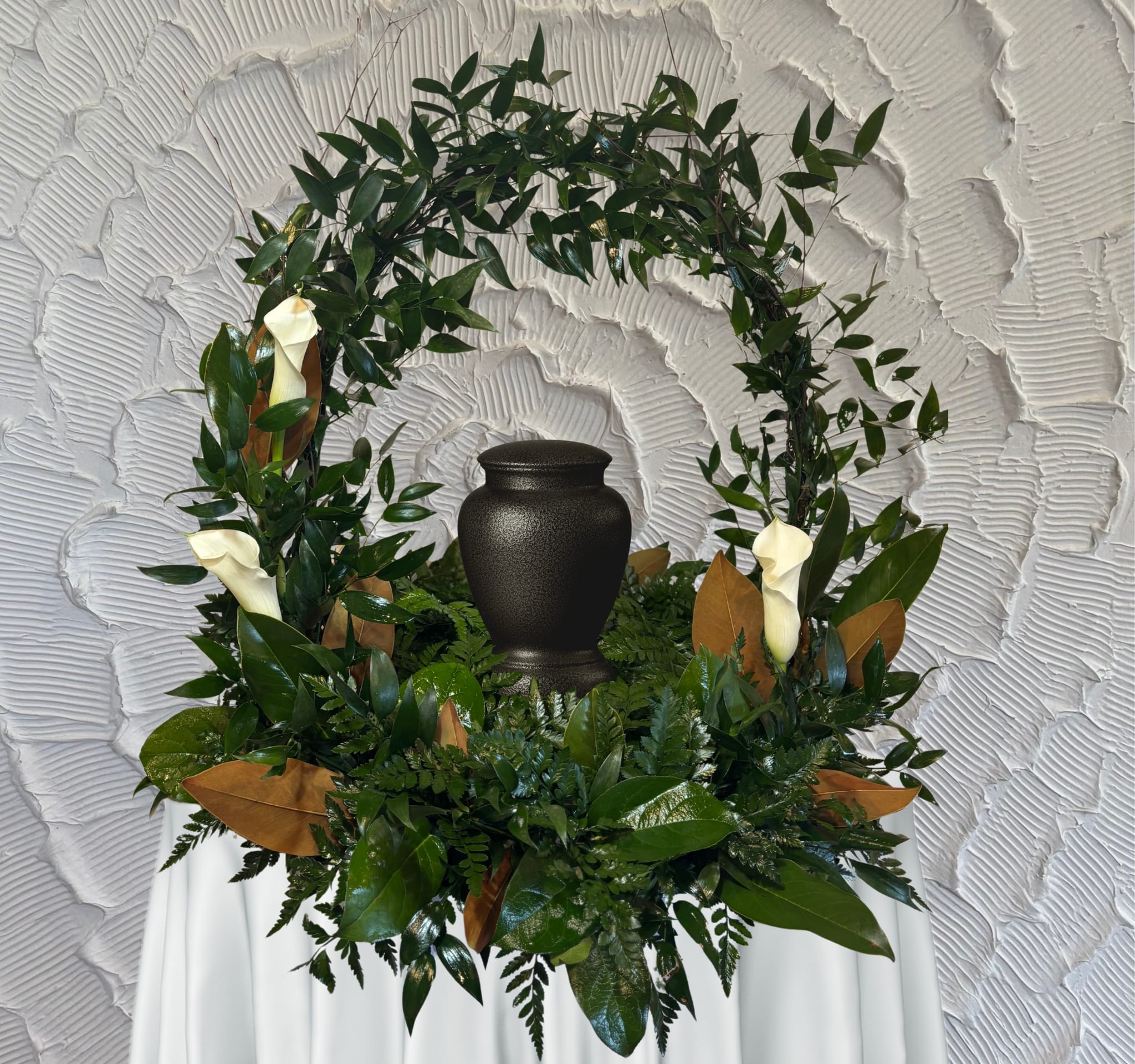 Green funeral wreath with white calla lilies around a black urn