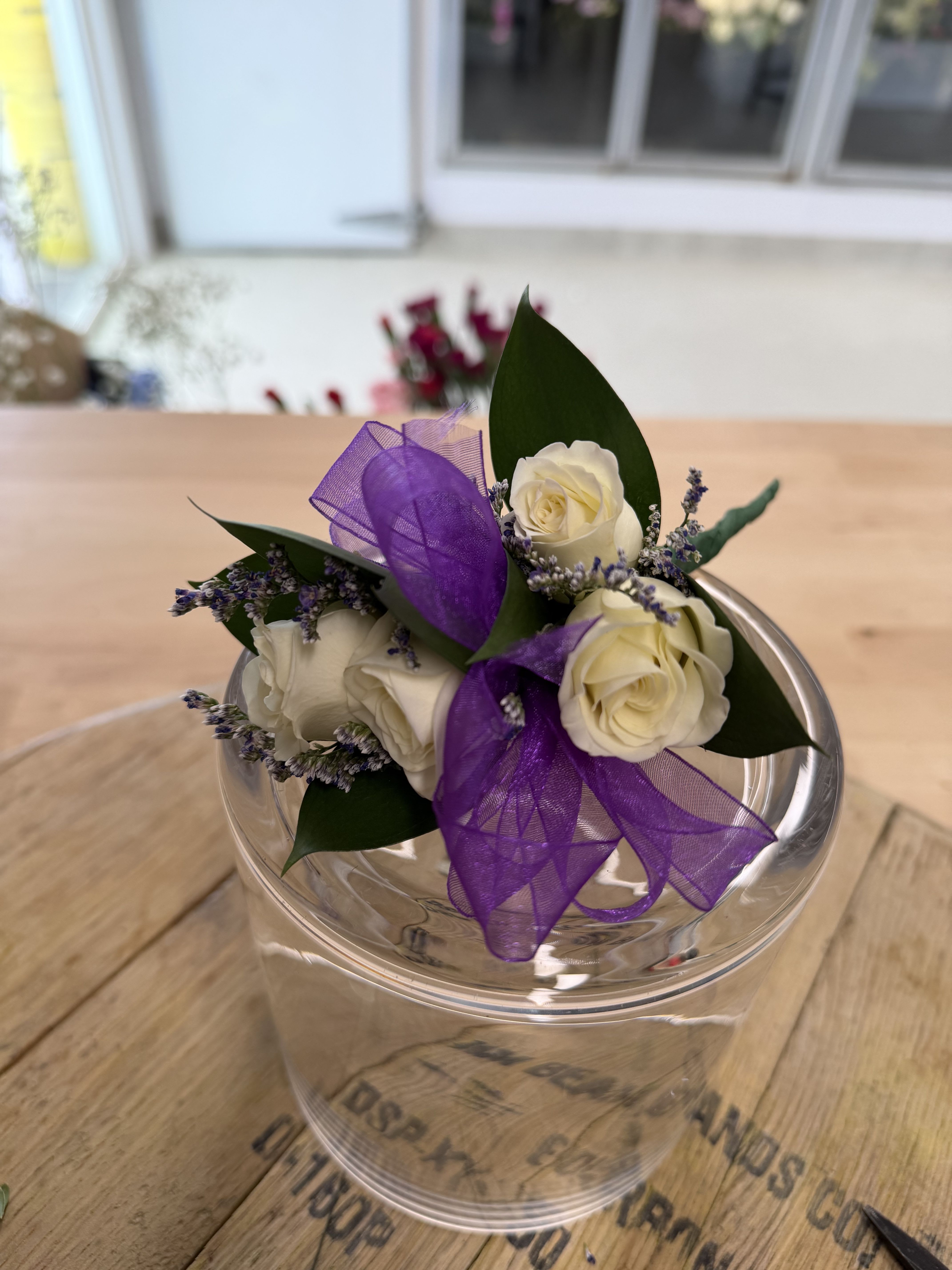 Small bouquet of white roses with purple ribbon in a clear container