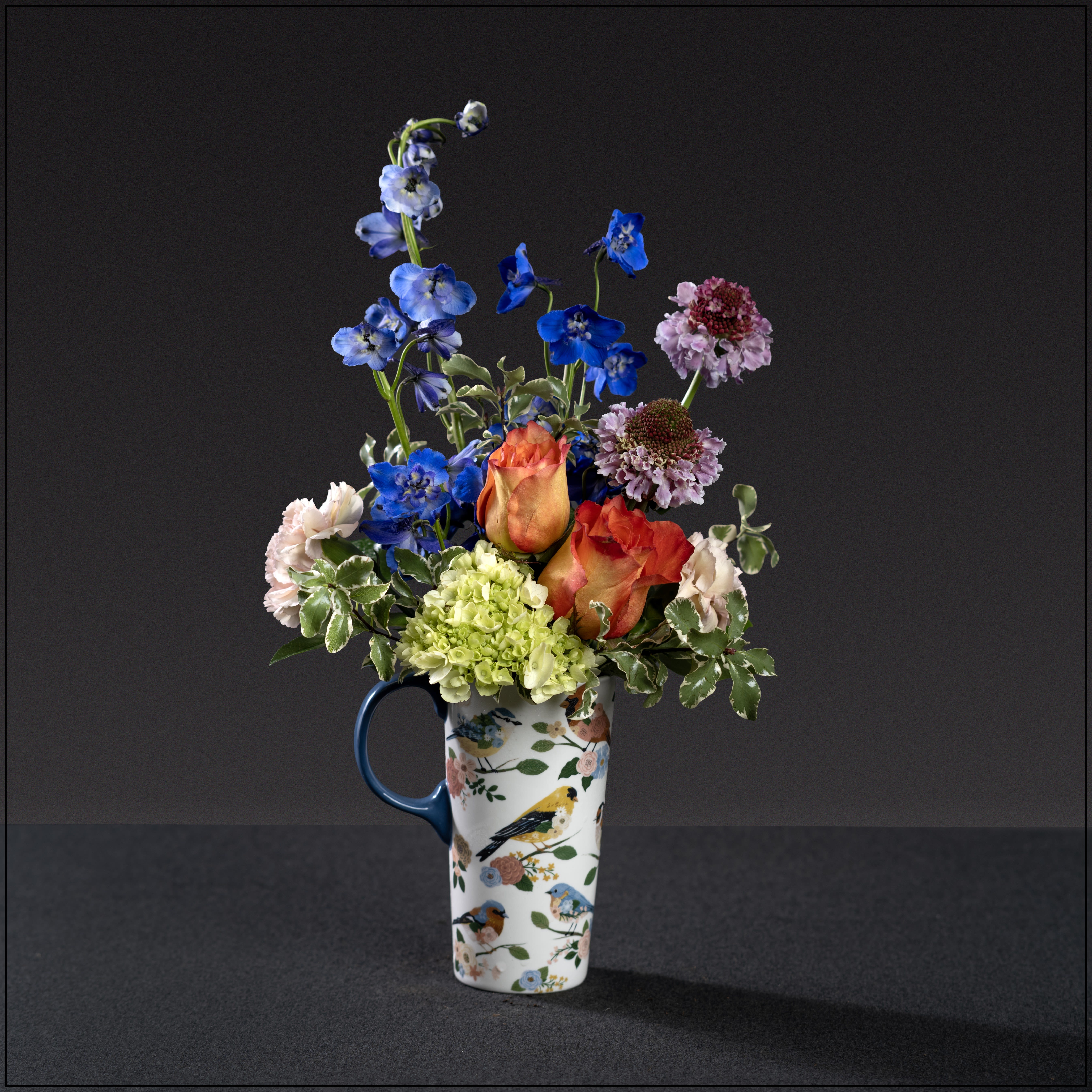 Birdies Garden Party - For the bird and nature lover.  A beautiful over-sized mug with graceful bird motif, filled with delphinium, miniature hydrangea, roses, and scabiosa. Approximately 18" tall and 9" wide.