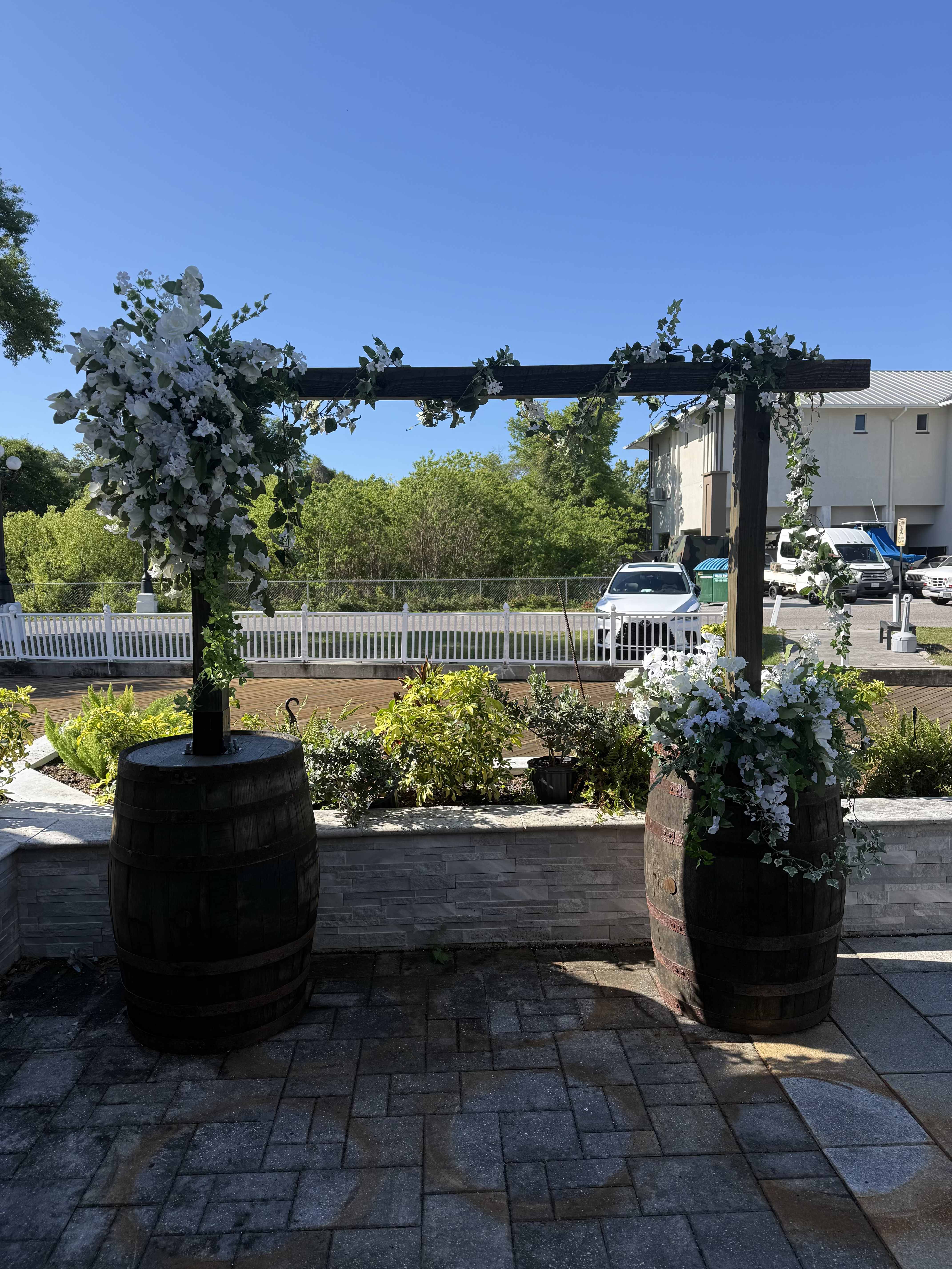 Barrel Arbor  - Wooden barrel arbor with a natural wood beam, styled with beautiful artificial flowers and greenery—perfect for a rustic ceremony backdrop. $350 – Arbor with floral $375 – Arbor with floral and draping RENT ONLY