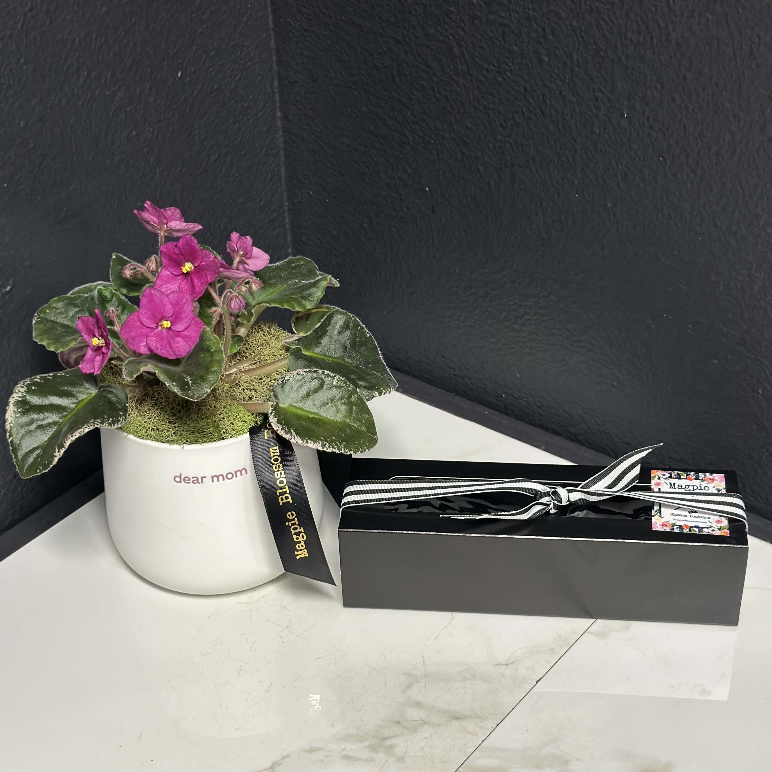 Dear Mom Violet Plant + Truffles  - Sometimes parents need a reminder that their kids (or plants) are turning out great. What better way than a daily reminder stamped in pink on a white glazed pot? With cheeky verbiage, beginning with "dear mom" on one side &amp; "good job, I turned out perfectly" on the other side. We've filled this simple, classic drop-in pot with a cute little plant and paired it with our delicious chocolate truffles for a great Mother's Day, birthday or just because gift. Plant/flower color may vary.  Pot size 4.25"x 4.25"