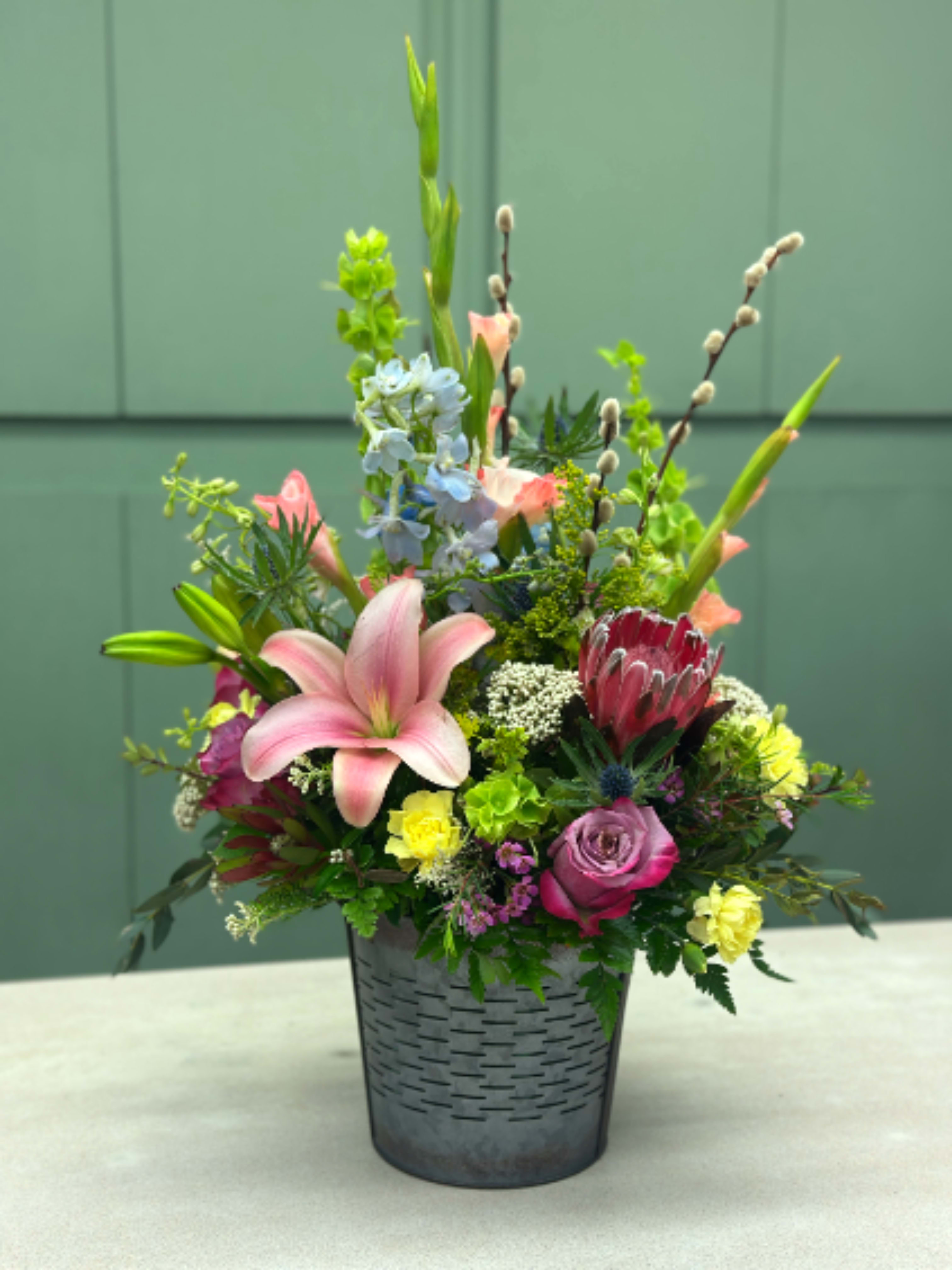 Spring Garden Bucket - Our Spring Garden Bucket features premium spring blooms in a keepsake galvanized garden bucket. The blooms in this arrangement may change, due to market availability, but the overall look and feel will be similar to the picture shown. 