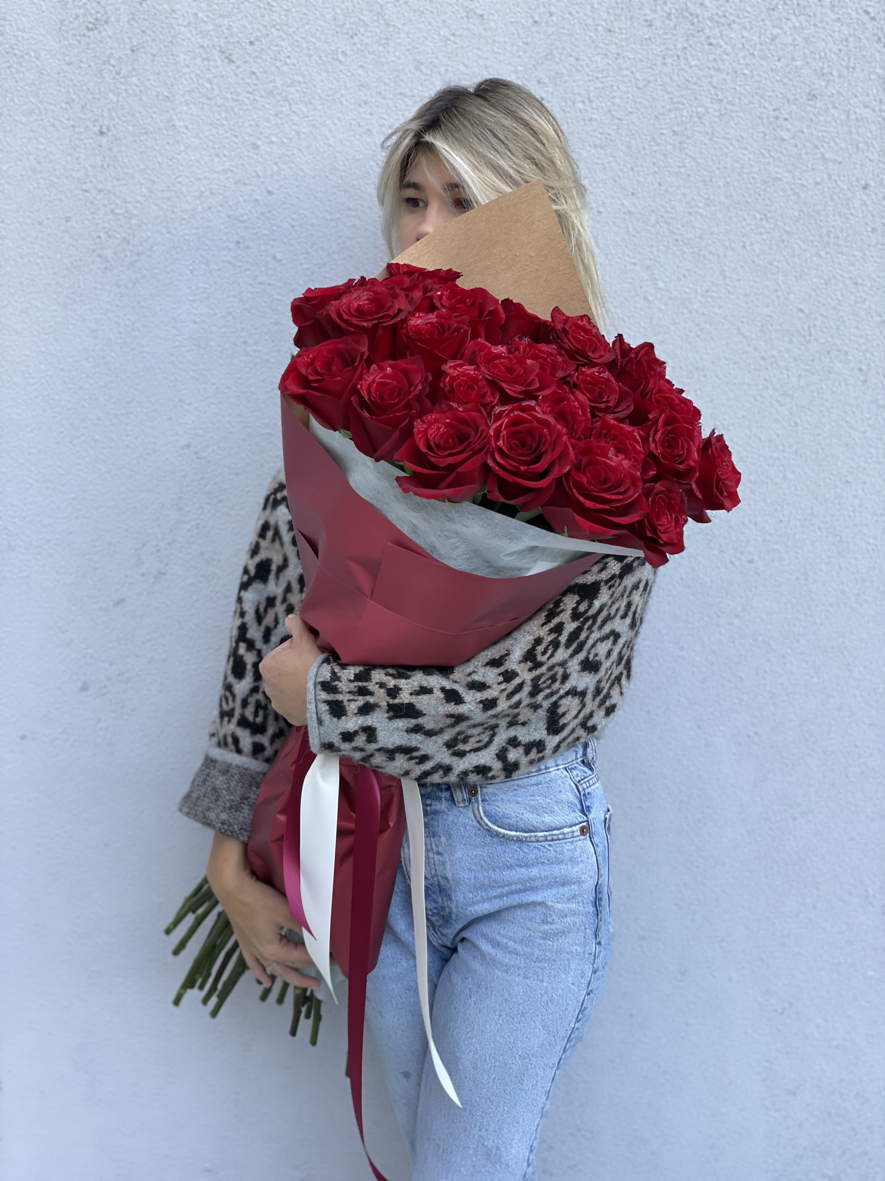 Bouquet of 25 stunning long stem red roses in a vase - A breathtaking bouquet of 25 premium long stem red roses, thoughtfully designed to make a bold and unforgettable statement. Each rose is hand-selected at peak freshness for its rich crimson hue, velvety petals, and elegant form, symbolizing deep love, passion, and timeless romance. Expertly arranged by our floral designers, this bouquet showcases the natural beauty of each bloom while creating a lush, full presentation that feels both classic and elevated.    The roses are beautifully wrapped in premium floral paper that enhances their dramatic color and refined style, making the bouquet stunning from every angle. Finished with elegant detailing, this arrangement is designed to impress the moment it’s received. Included with the bouquet is a clear glass vase, allowing for effortless display and long-lasting enjoyment at home or in the office.    Perfect for anniversaries, romantic milestones, Valentine’s Day, or when words simply aren’t enough, this bouquet delivers an unmistakable message of love and devotion. Whether you’re celebrating a special occasion or creating an unforgettable surprise, these 25 long stem red roses offer a luxurious floral experience that speaks straight from the heart.