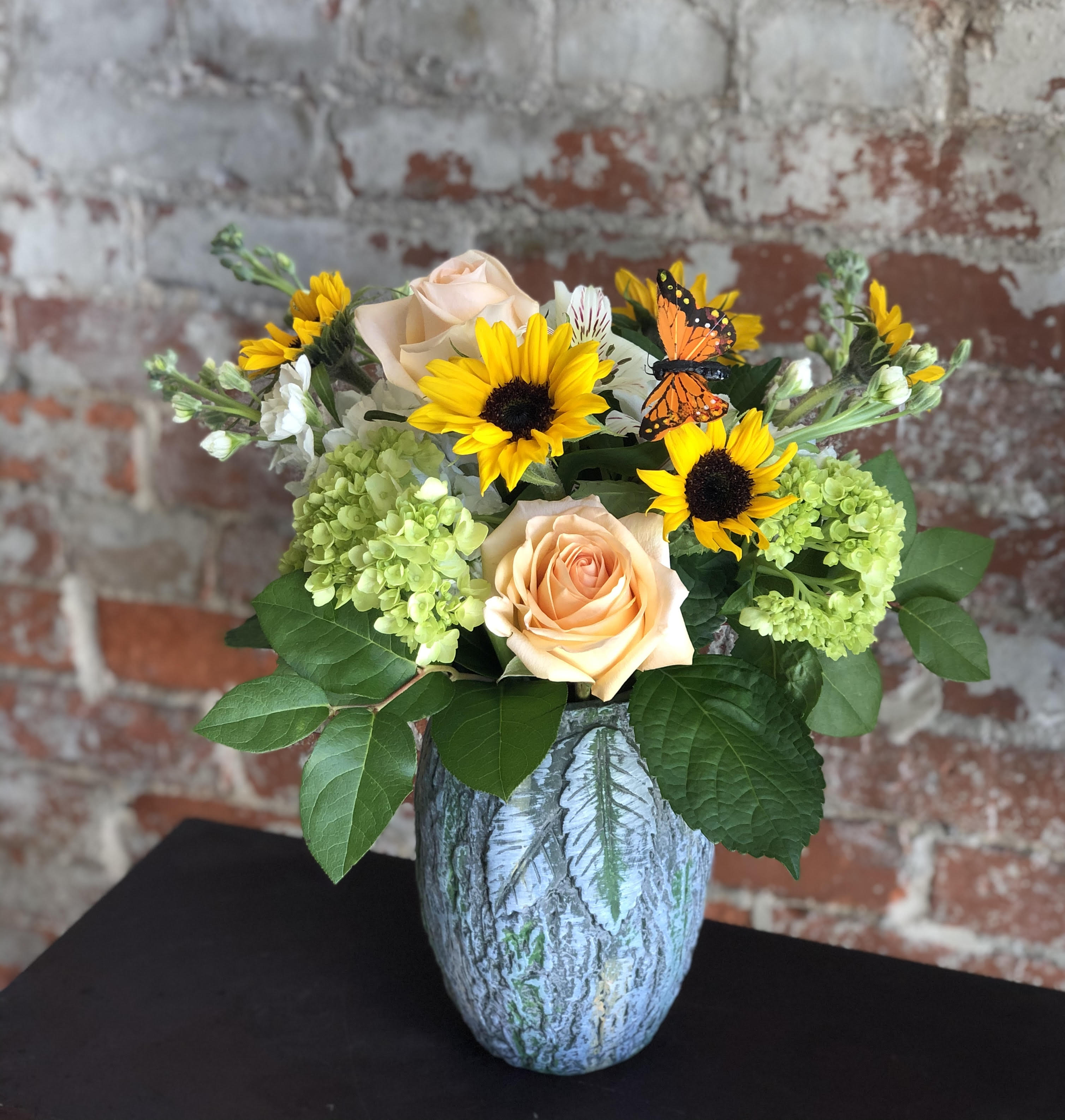 Peach roses and yellow sunflowers in a blue vase with butterfly accents