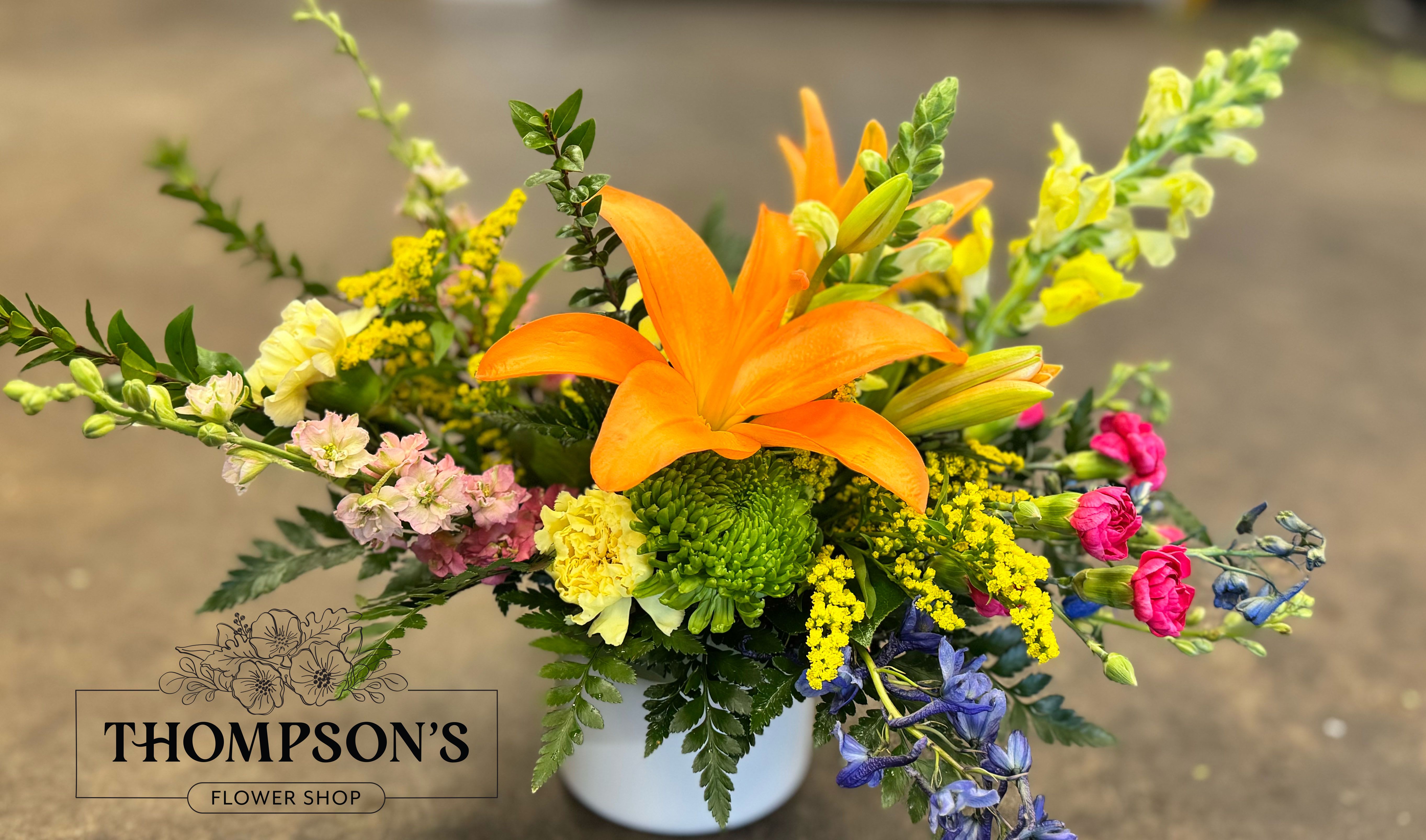 Devotion - Designed to honor the love that shows up in a thousand quiet ways, Devotion is a heartfelt expression of appreciation. Centered around a striking orange lily and surrounded by vibrant seasonal blooms in warm, uplifting tones, this arrangement feels both bold and deeply meaningful. Thoughtfully arranged in a modern ceramic cylinder, it’s a beautiful way to celebrate everything Mom is and everything she gives. Available exclusively for Mother’s Day week.