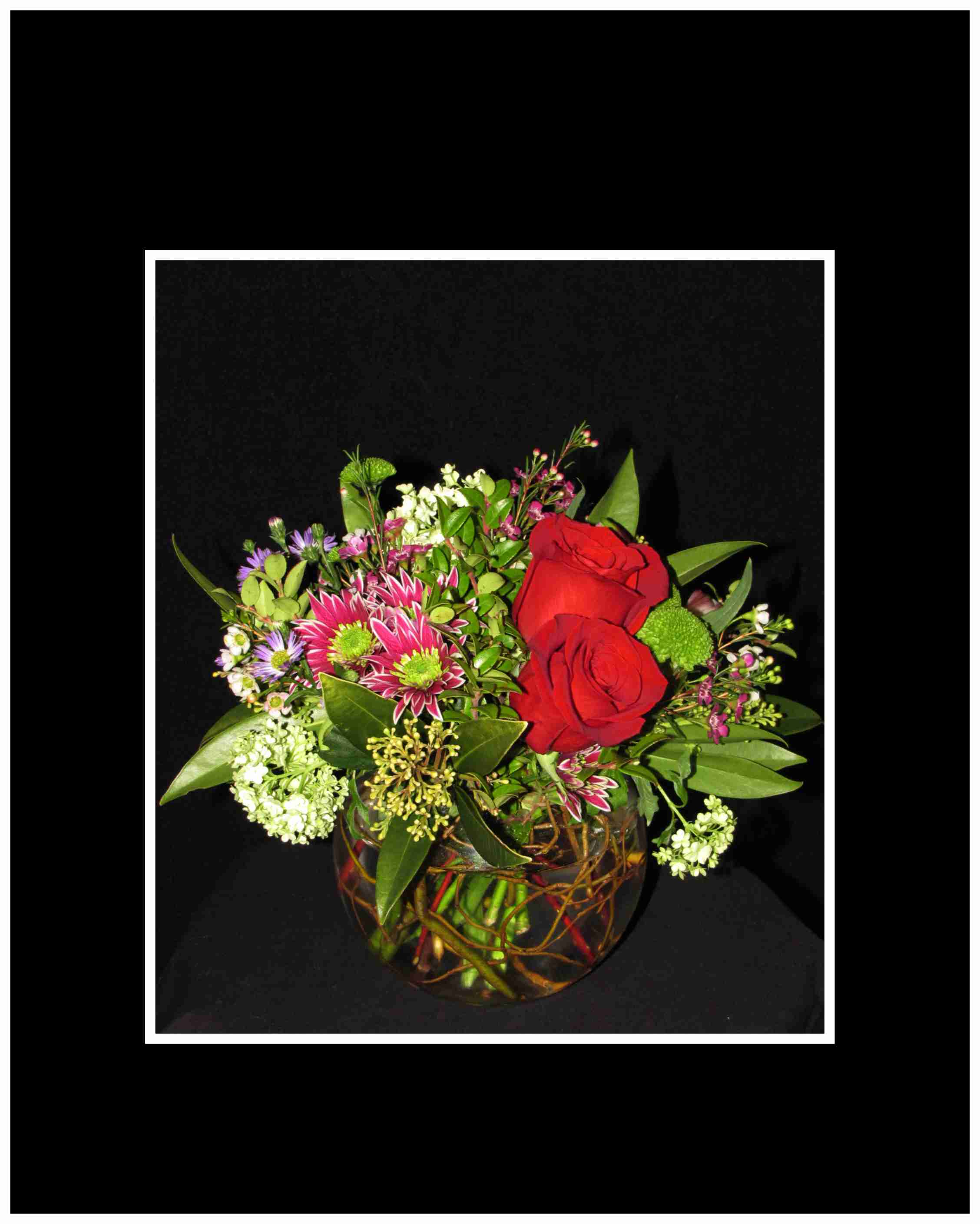 Red roses and mixed flowers arranged in a round glass vase