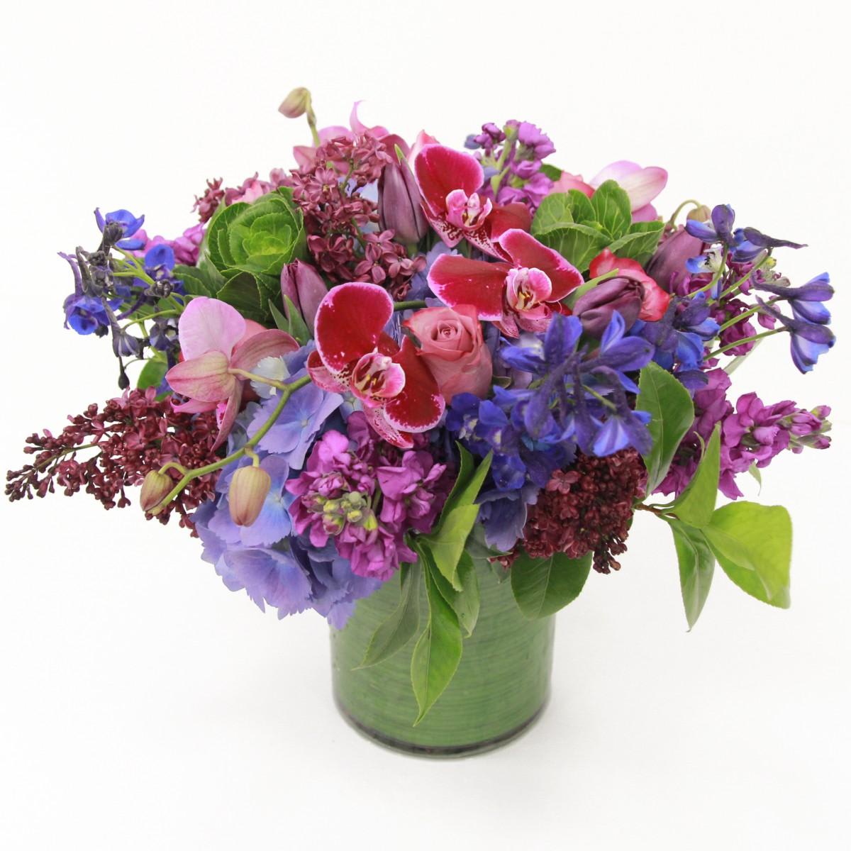    Gorgeous Luxury Bouquet - A thoughtful and truly wonderful way to let a friend or family member know you’re thinking of them. This beautiful arrangement features bright seasonal stems, perfect to lift the spirits and add a pop of colour to the home. A perfect way to send love and brighten someone’s day.  brilliantly colorful short cylinder vase filled with blue delphinium, exotic burgundy phaleanopsis orchids, pink stock, lavender roses, lilacs