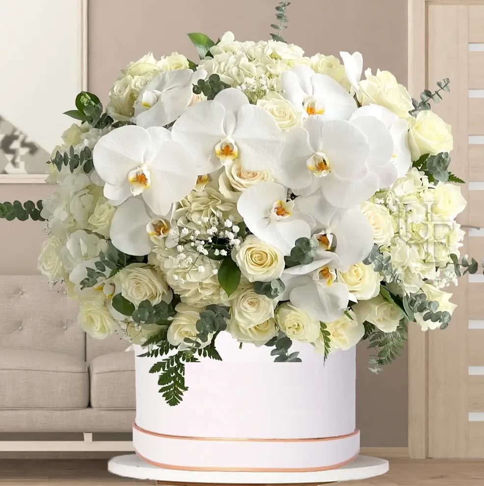 Large white floral arrangement with orchids and roses in a round box