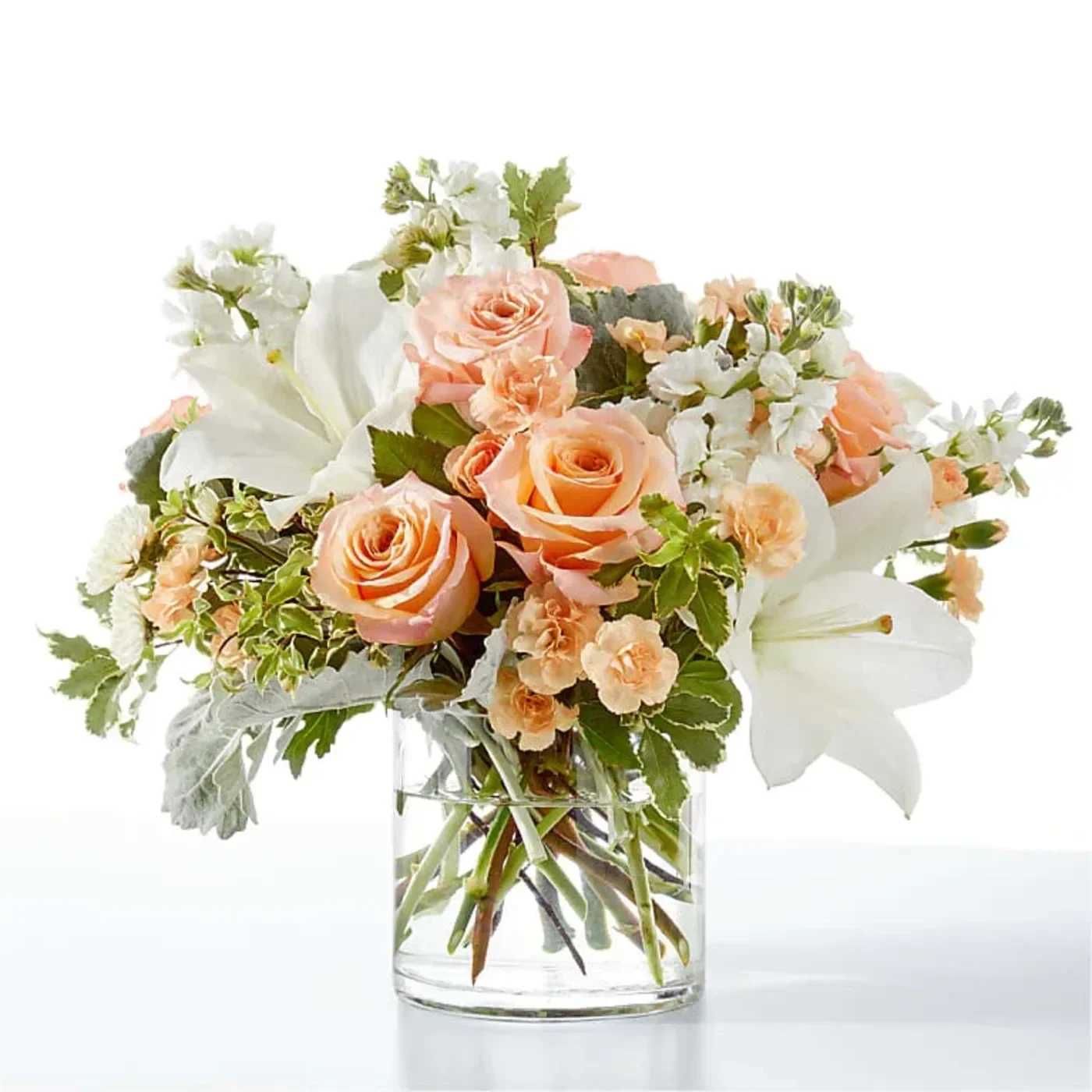 Peach roses and white lilies in a clear glass vase