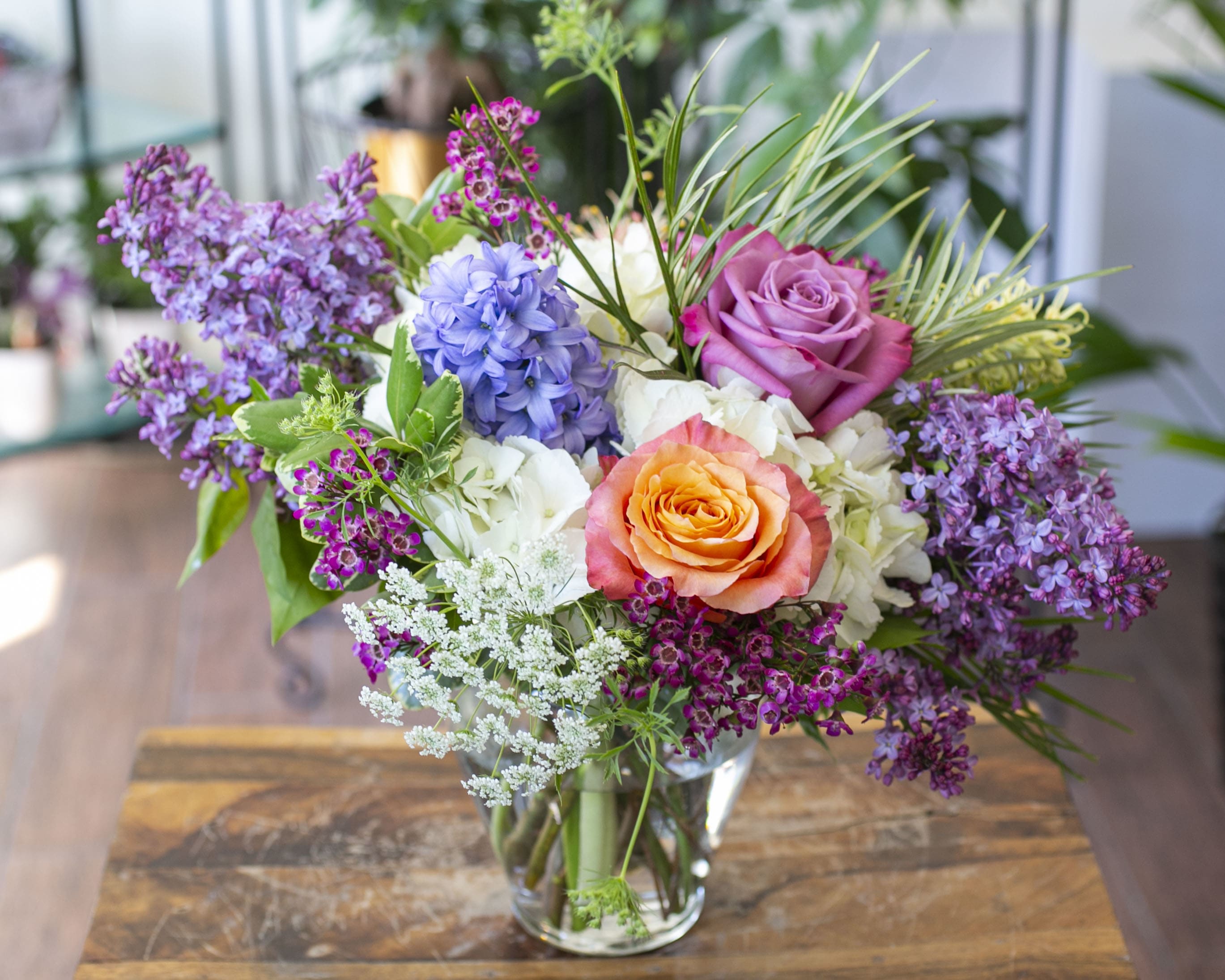 Mixed bouquet of roses, hydrangea, and purple blossoms in a clear glass vase