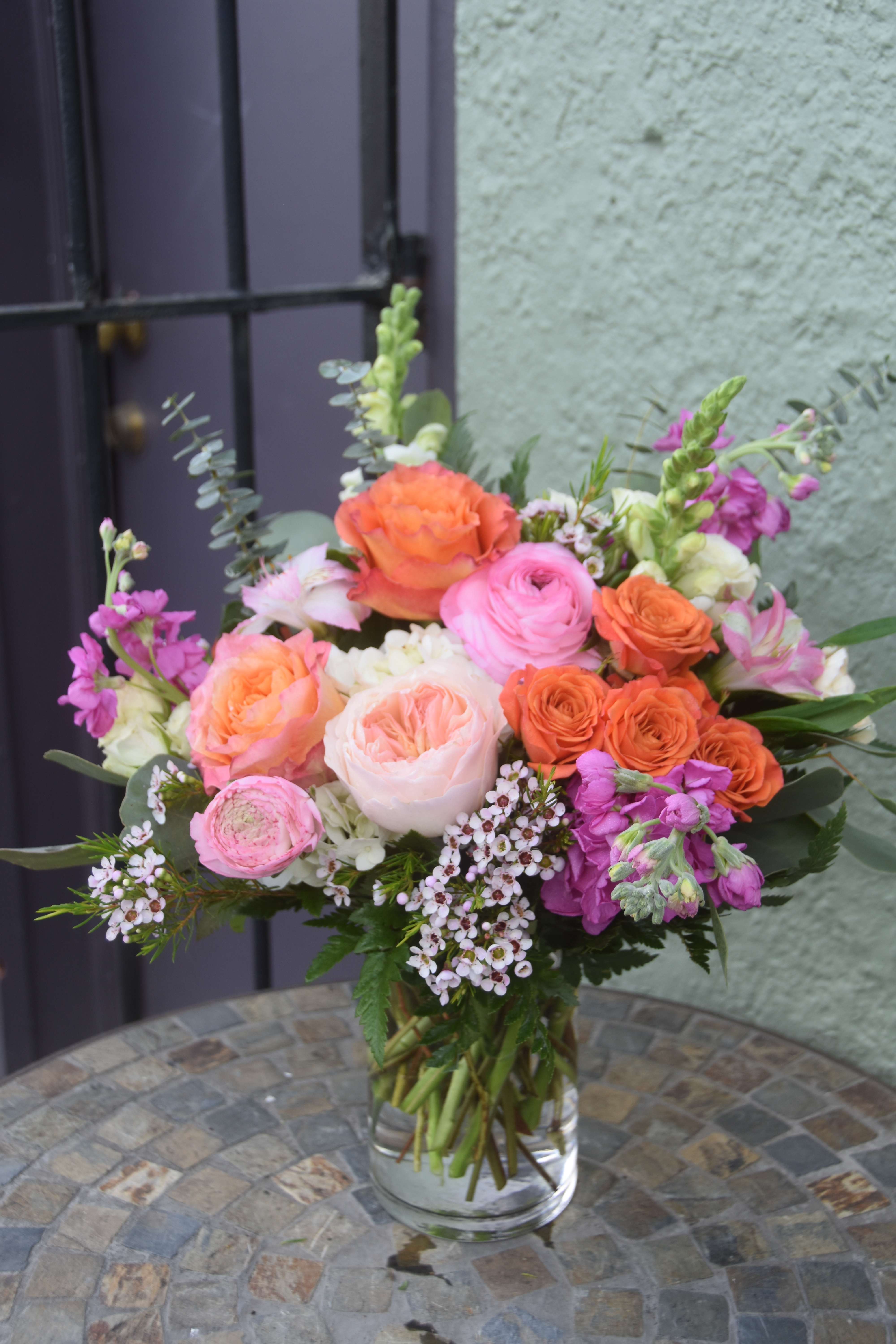 Mixed bouquet of pink and orange roses and other flowers in a clear glass vase