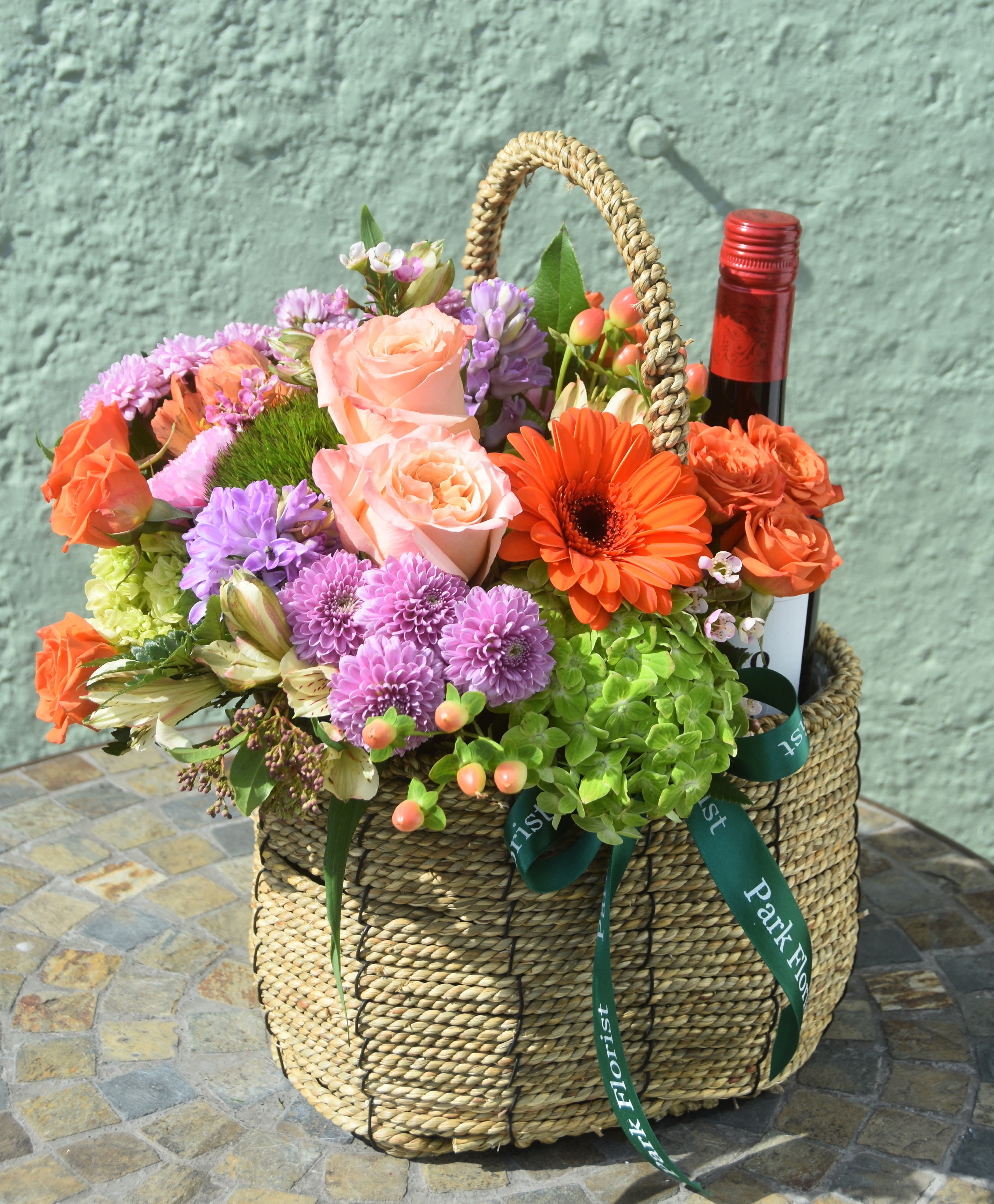 Woven basket of mixed colorful flowers with a wine bottle tucked among the blooms