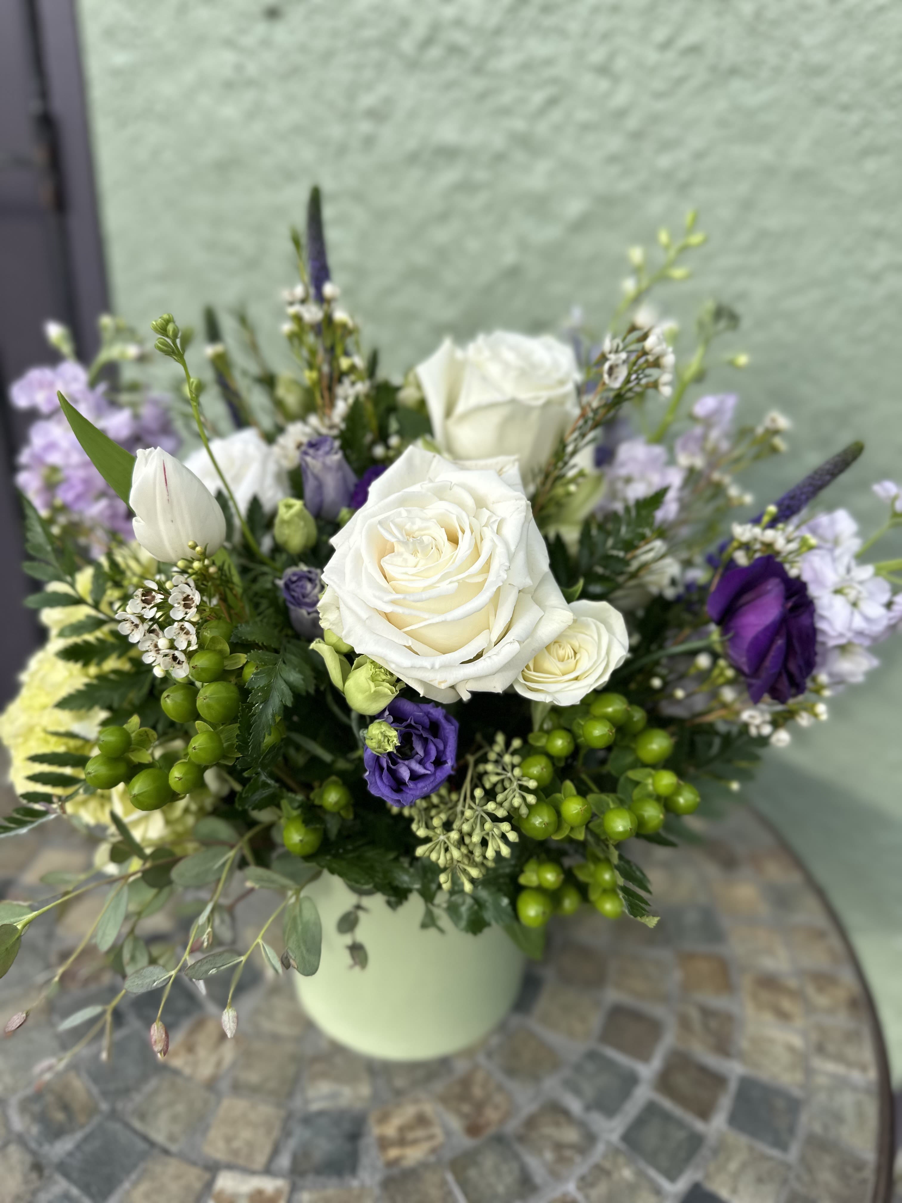 Arrangement of white roses and purple flowers in a light green vase on a mosaic table