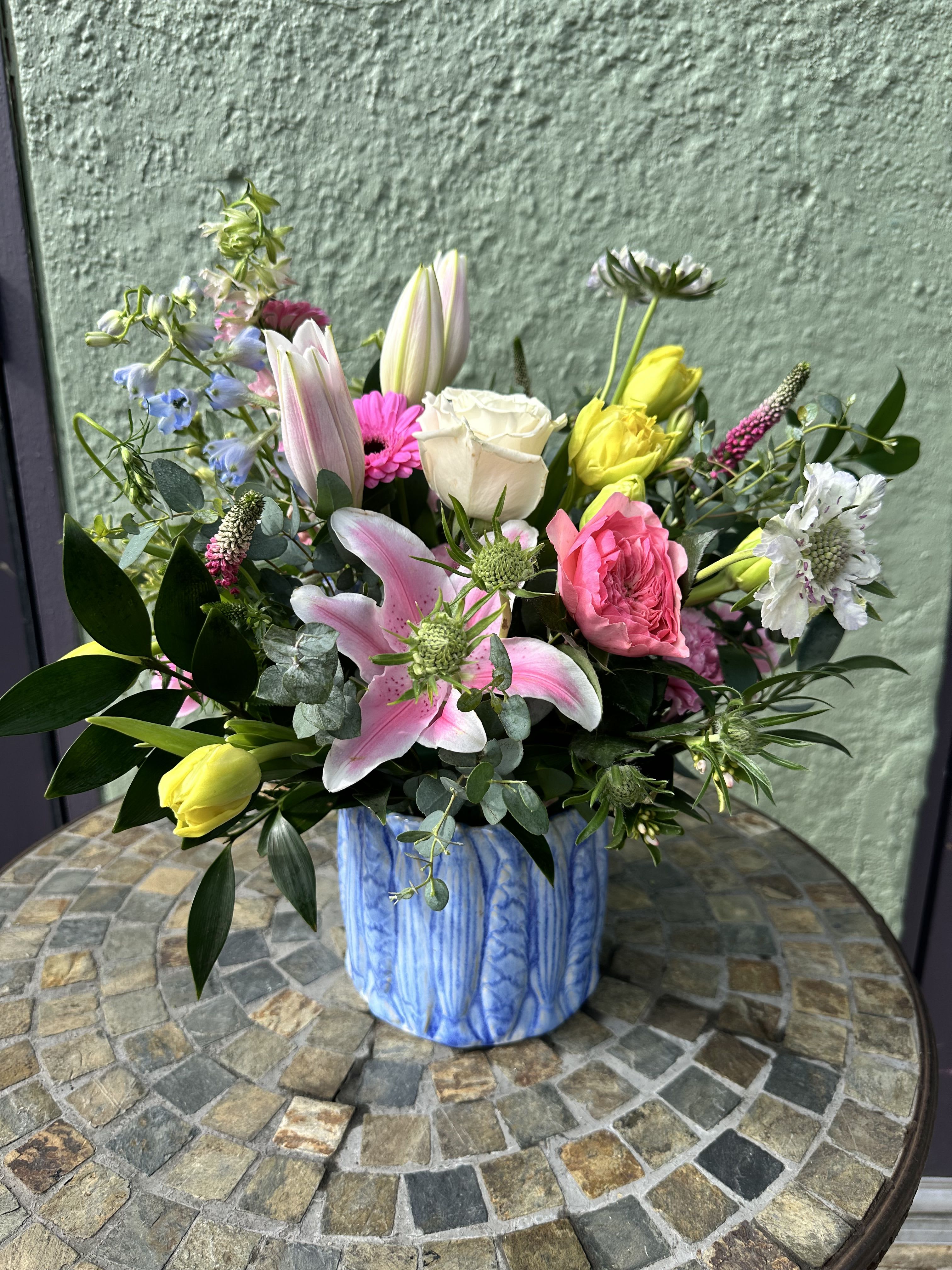 Colorful mix of lilies, roses, tulips and other blooms in a blue ceramic vase