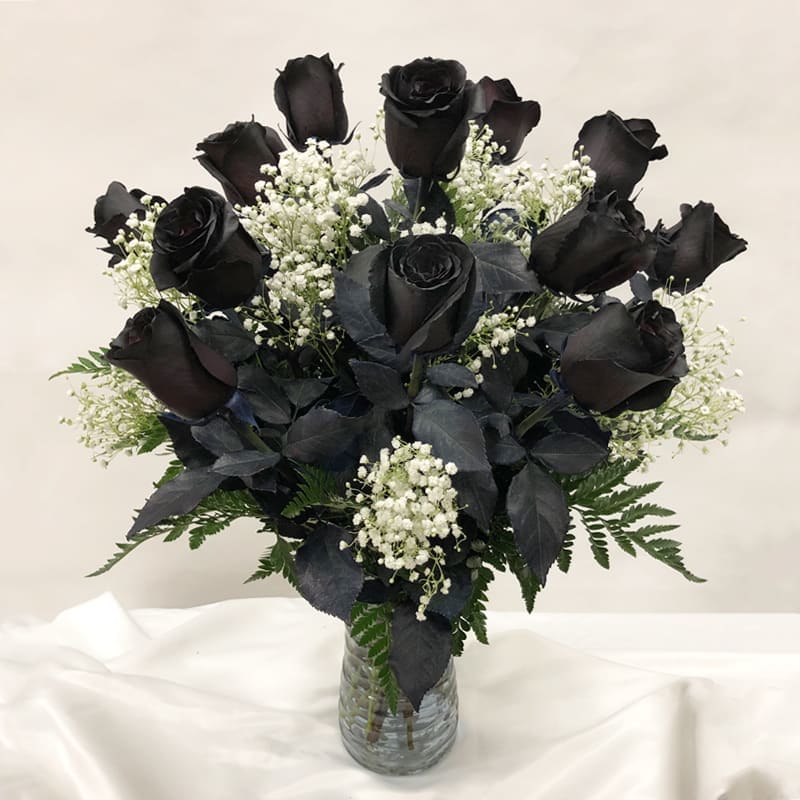 Arrangement of black roses with white filler flowers in a clear glass vase
