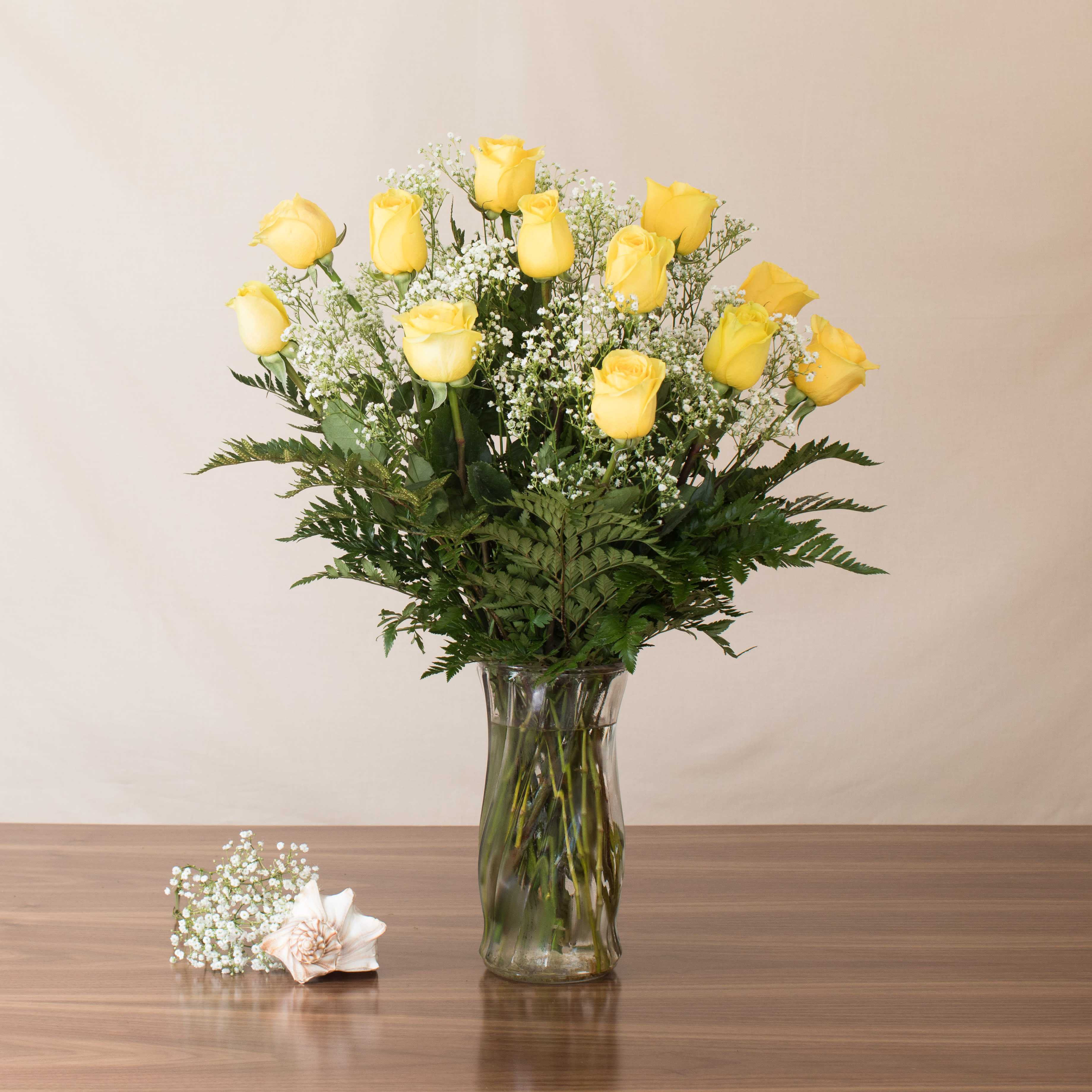 Tall arrangement of yellow roses with white accent flowers in a clear glass vase