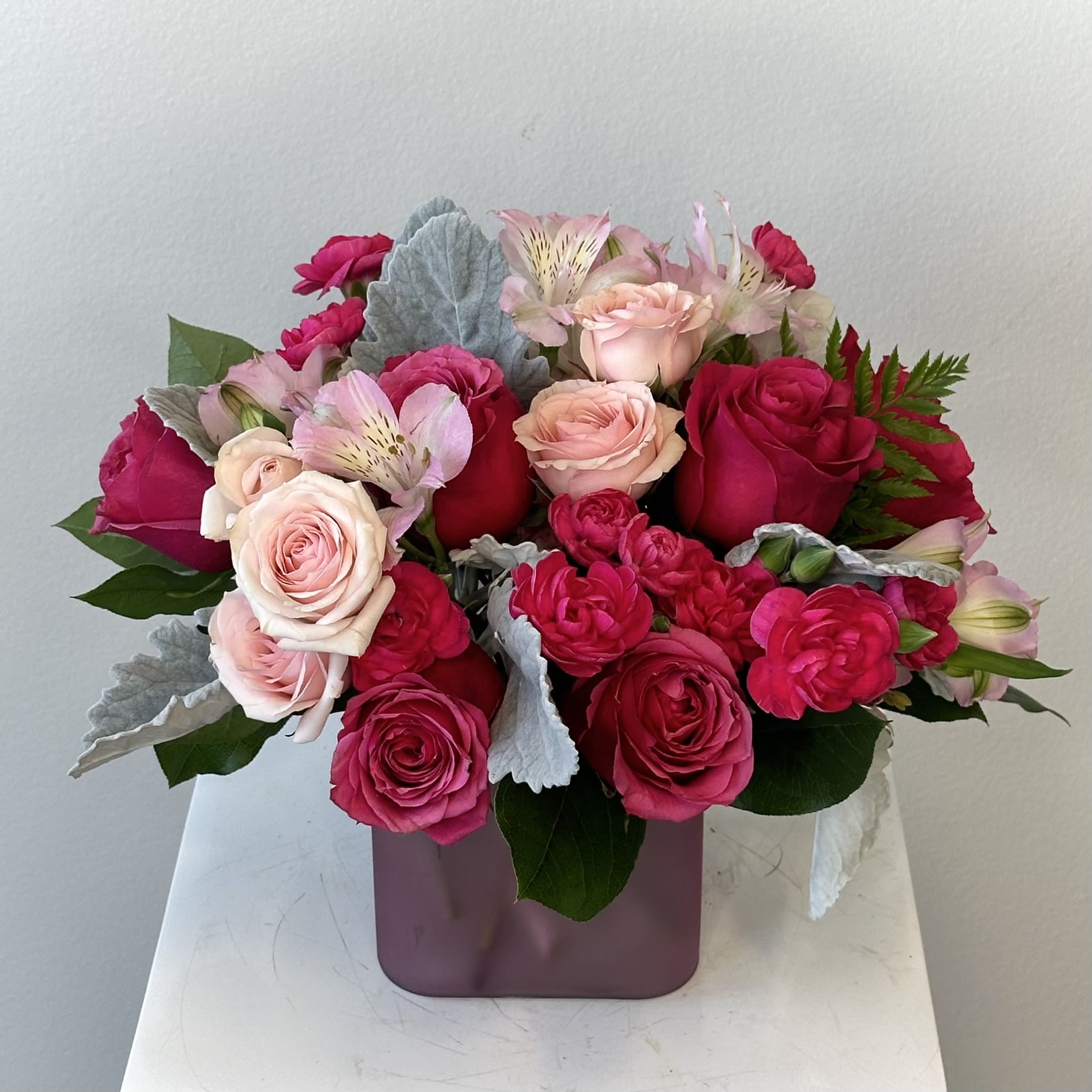 Compact arrangement of hot pink and blush roses with pink alstroemeria in a mauve cube vase