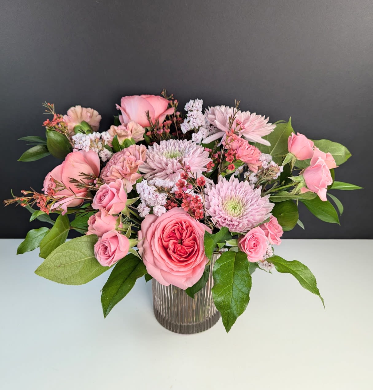 Pink roses and chrysanthemums arranged in a ribbed glass vase