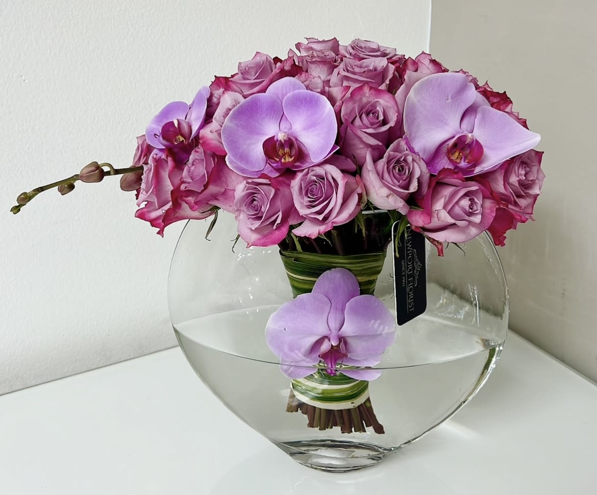 Pink roses and lavender orchids arranged in a clear glass vase