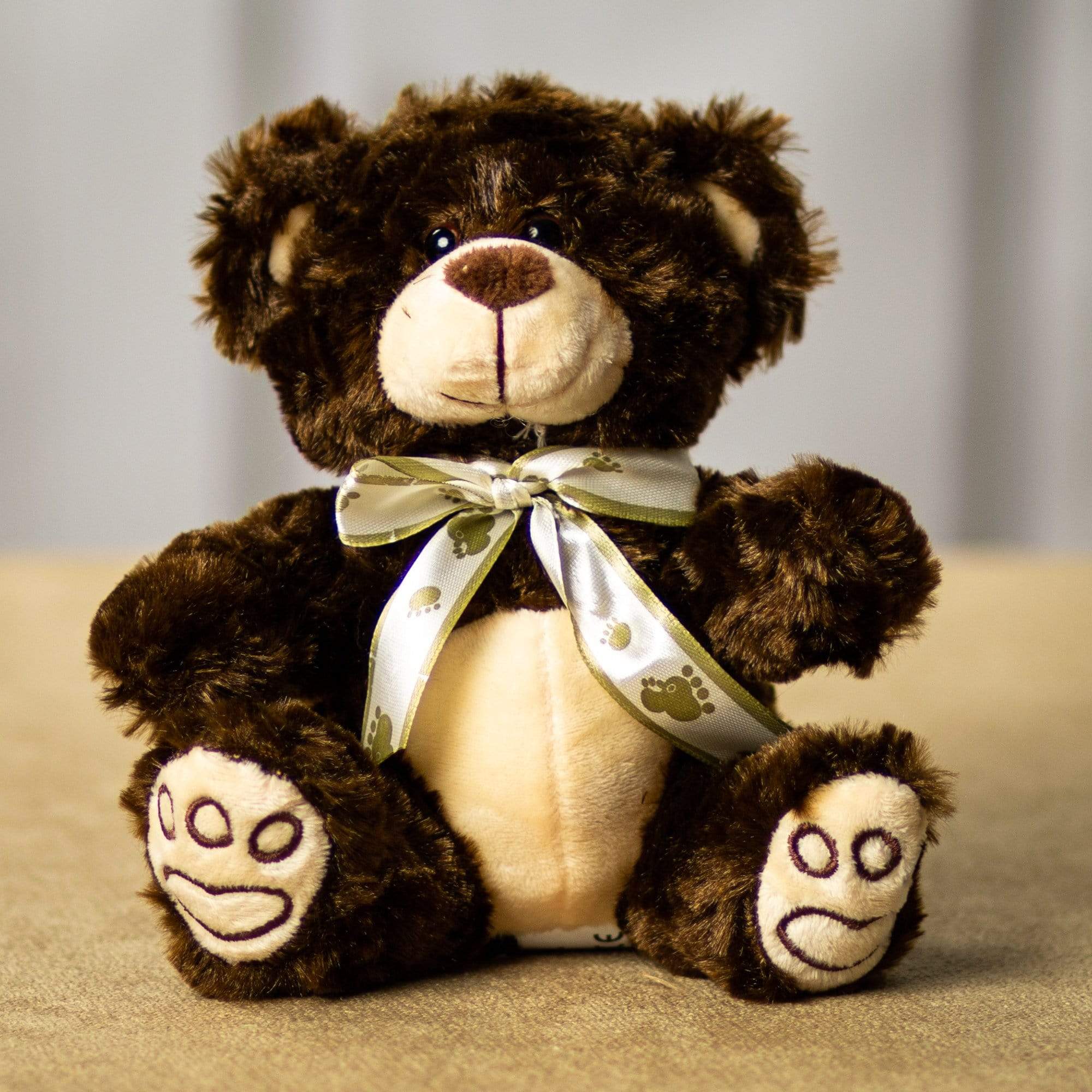 Brown teddy bear with a ribbon bow sitting on a neutral surface