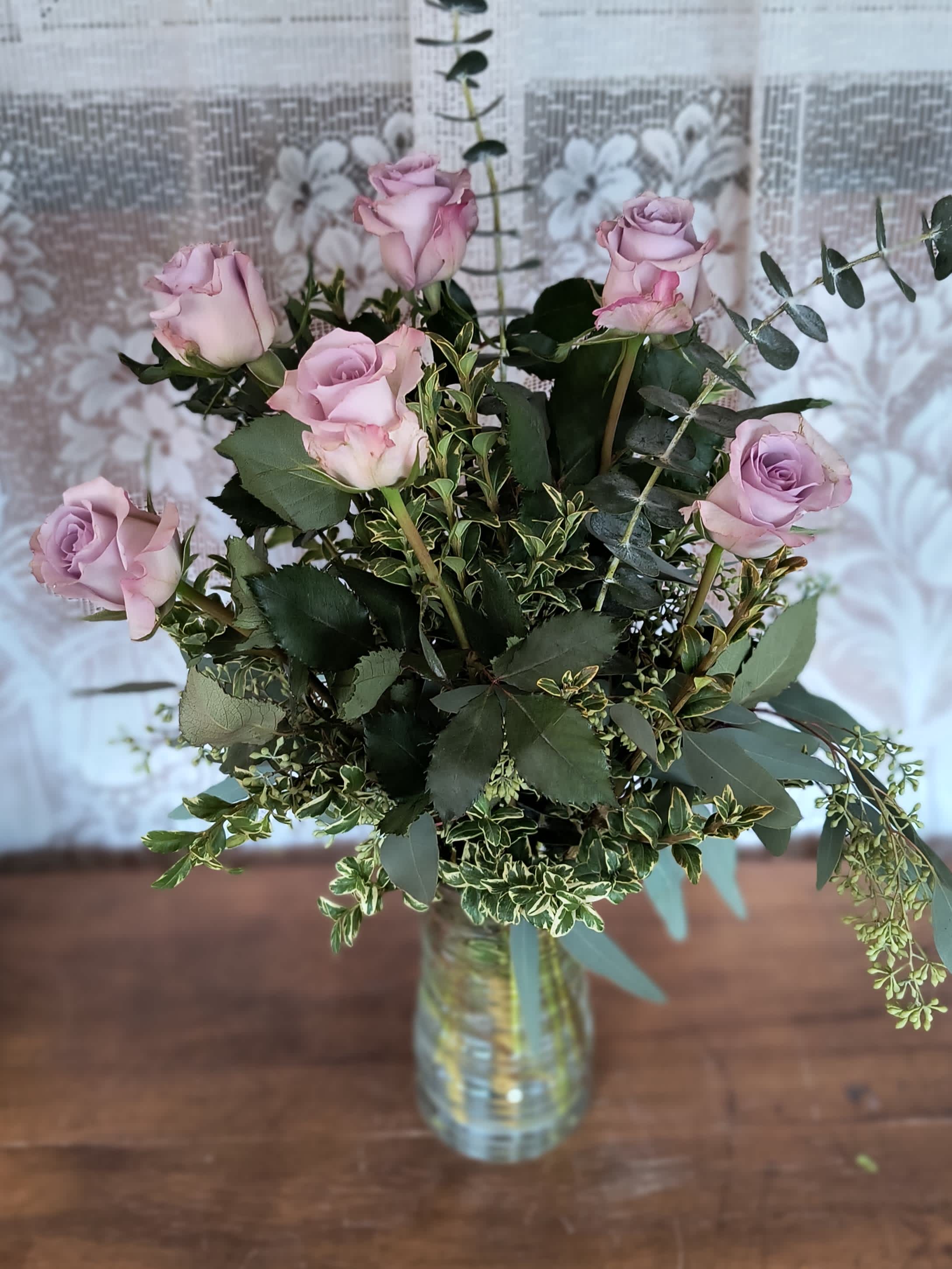 Lavender roses arranged in a clear glass vase with mixed greenery